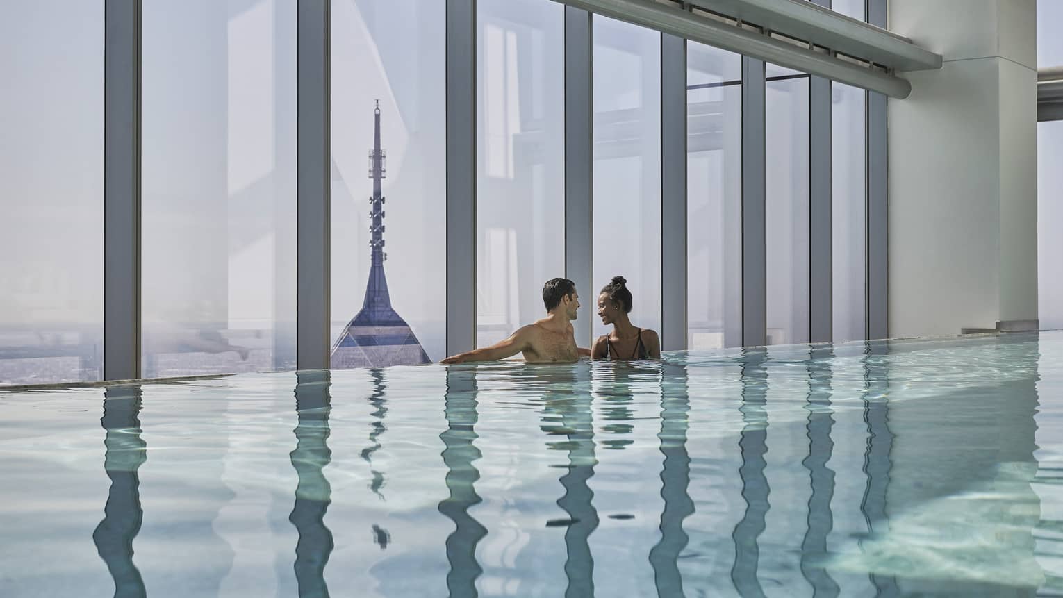 A man and woman stand close to one another in the pool overlooking downtown Philadelphia