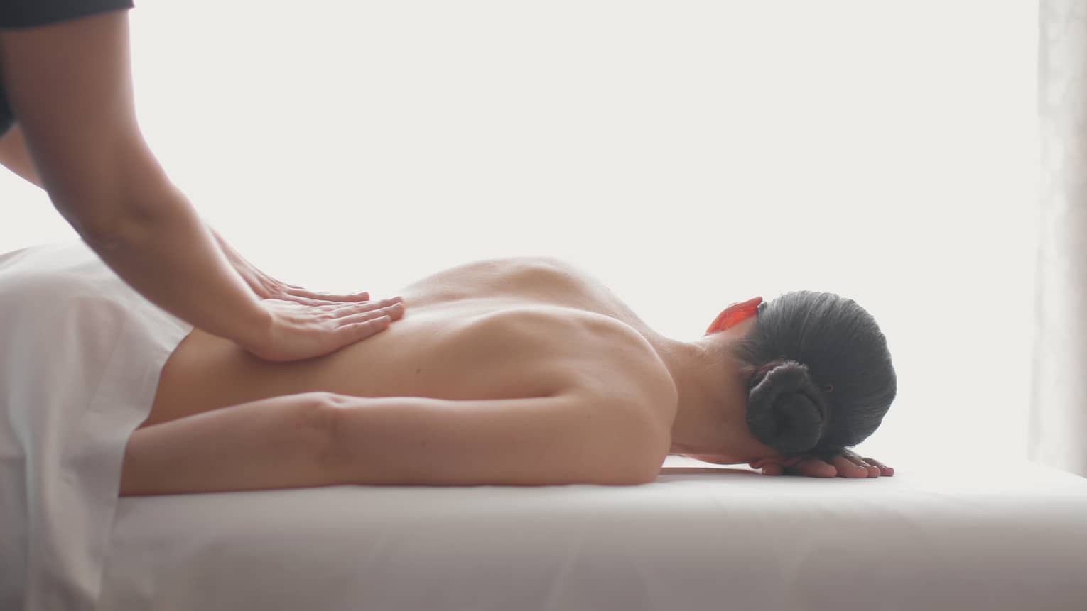 Side view of woman lying on massage table, hands massaging her bare shoulders