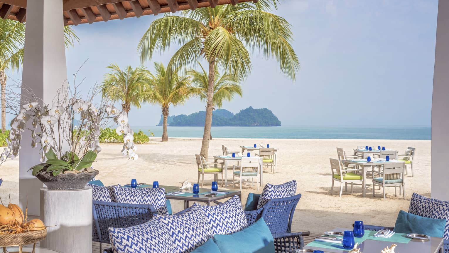 Terrace of ocean-view restaurant, blue cushions on sofa, turquoise place mats and blue glasses on table