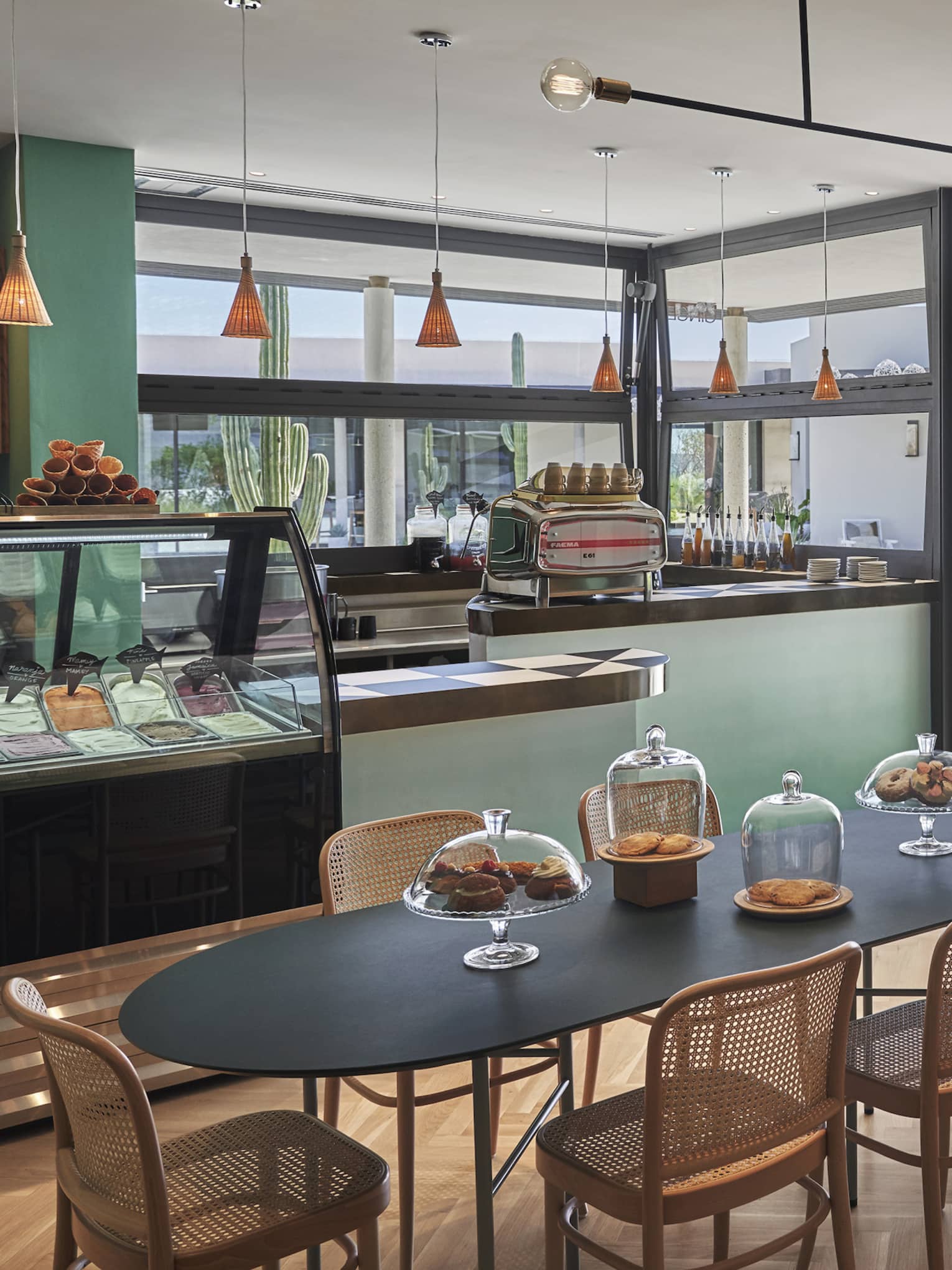 Green-walled Gingers dining area, black oval table and wicker chairs, food display case