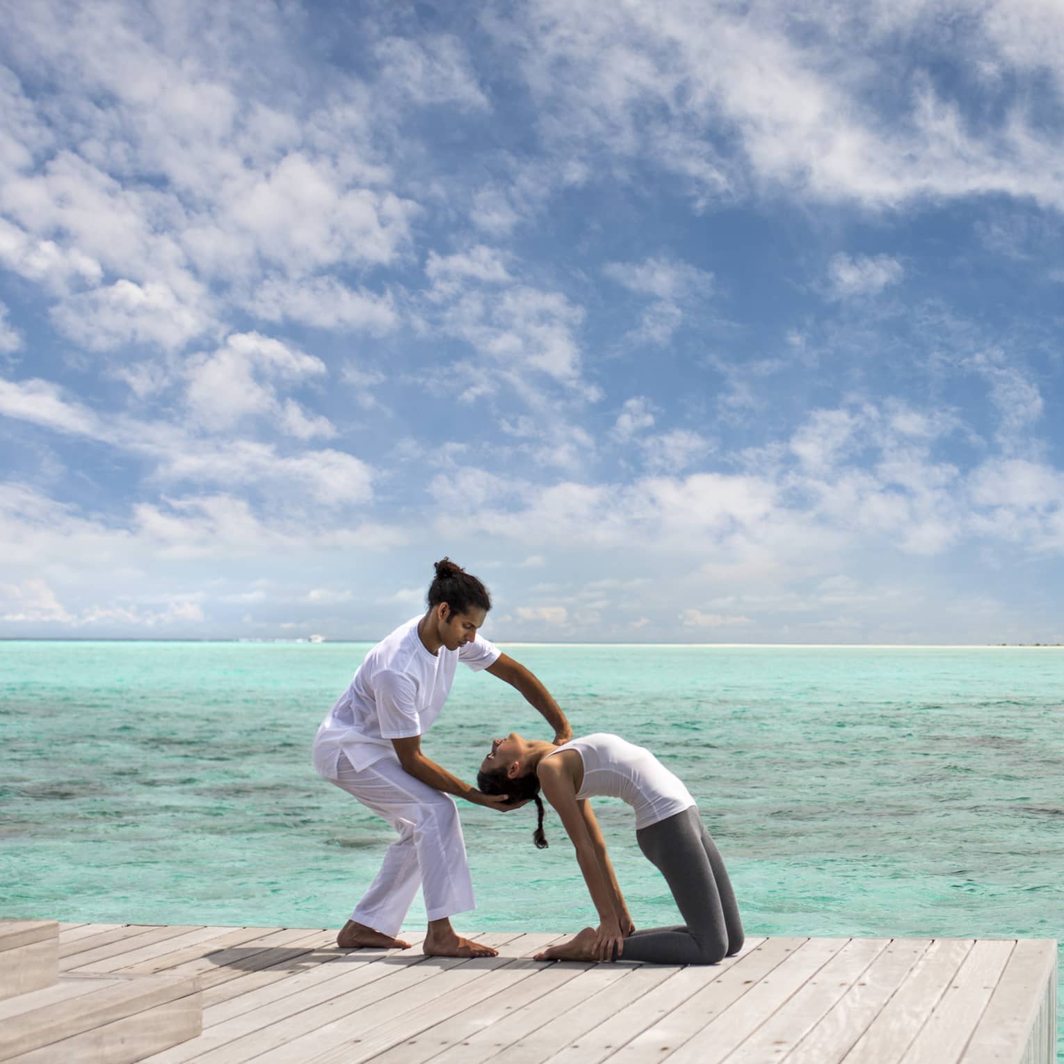 Woman leans back into hands of Yoga Therapist on dock over lagoon