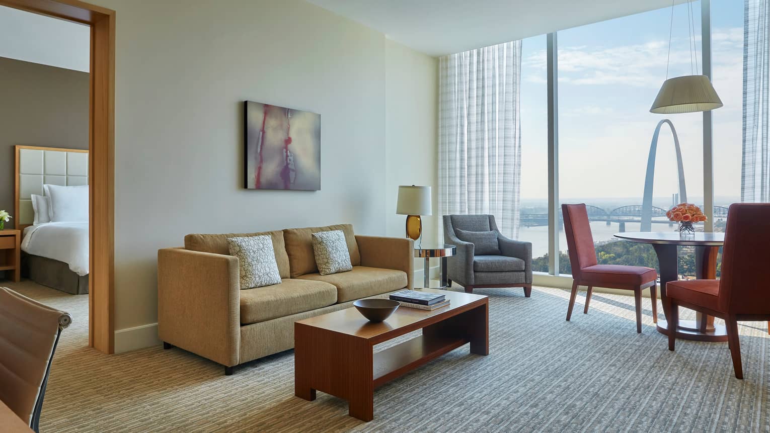Arch one-bedroom suite living room with gold sofa, grey armchair and dining table, near separate bedroom