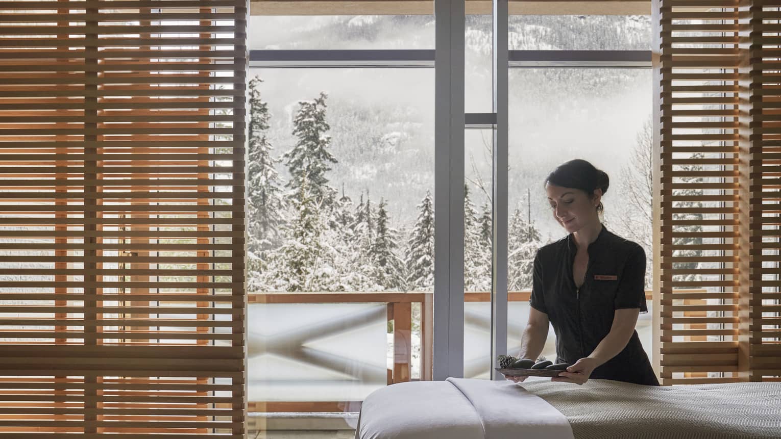 Spa staff smooths sheet on massage table in front of window with winter view