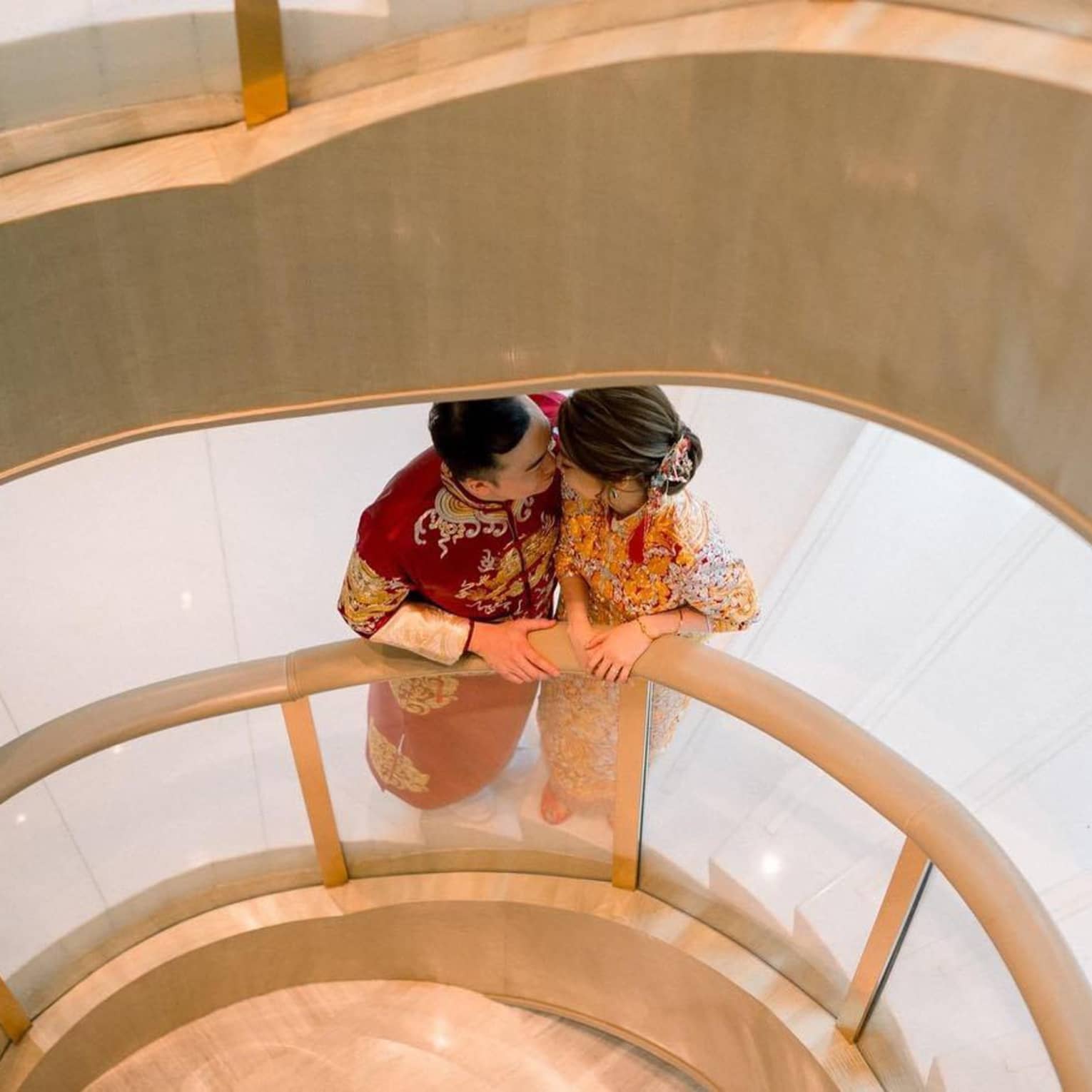 A couple share a kiss on a spiral staircase dressed in wedding attire. 