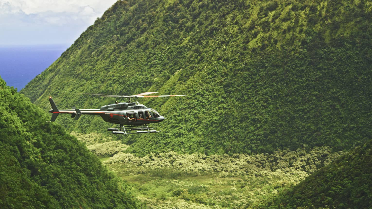 Orange and grey helicopter flying through crevice between green mountains