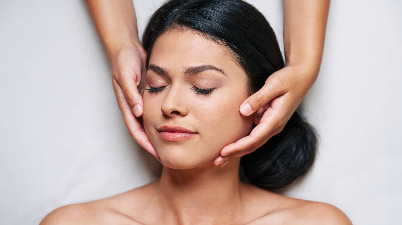 Woman with eyes closed as hands massage her face