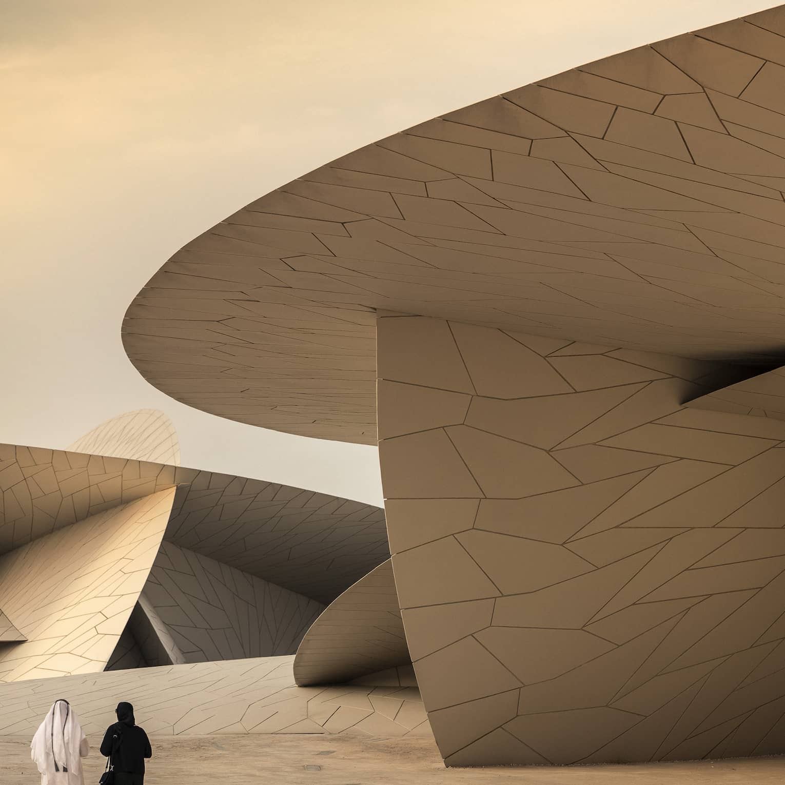 Two people walk beside a giant modern structure featuring large, overlapping, disc-shaped forms with geometric patterns. 