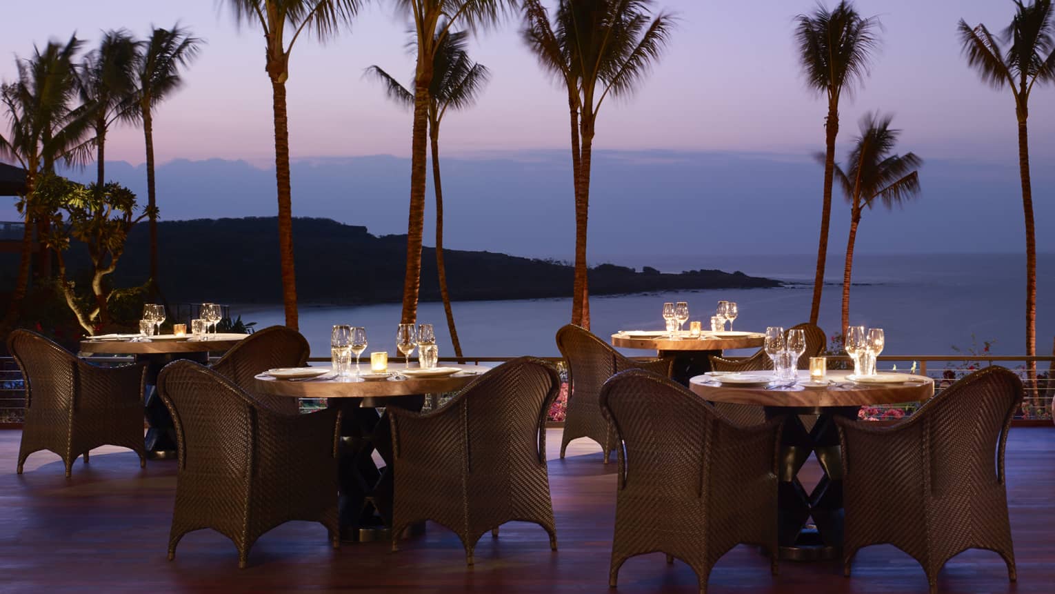 Wicker dining chairs around patio tables overlooking beach on One Forty patio at night