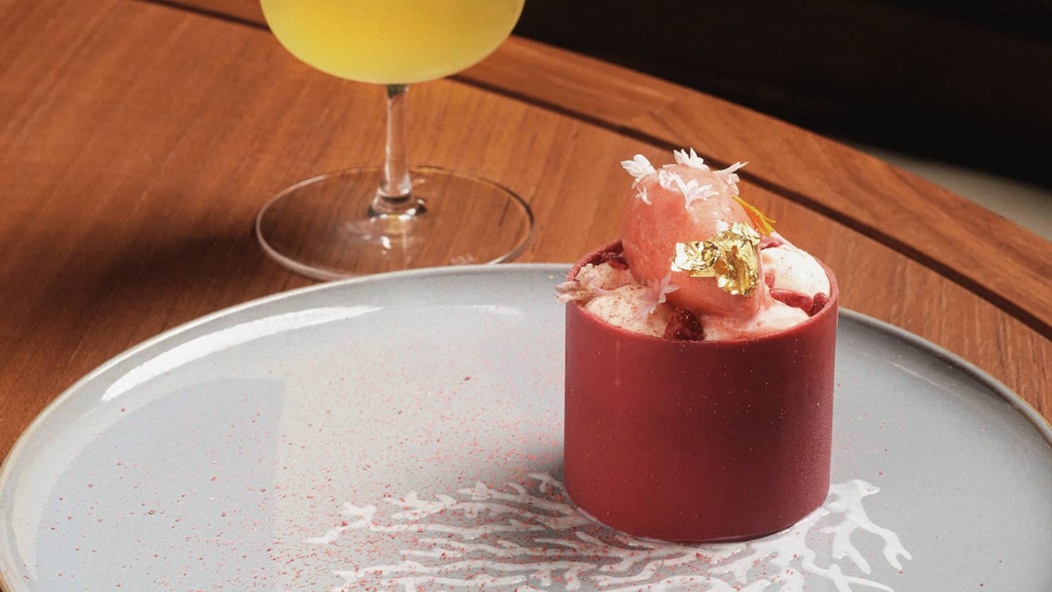 A small strawberry cake on a grey plate beside a cocktail