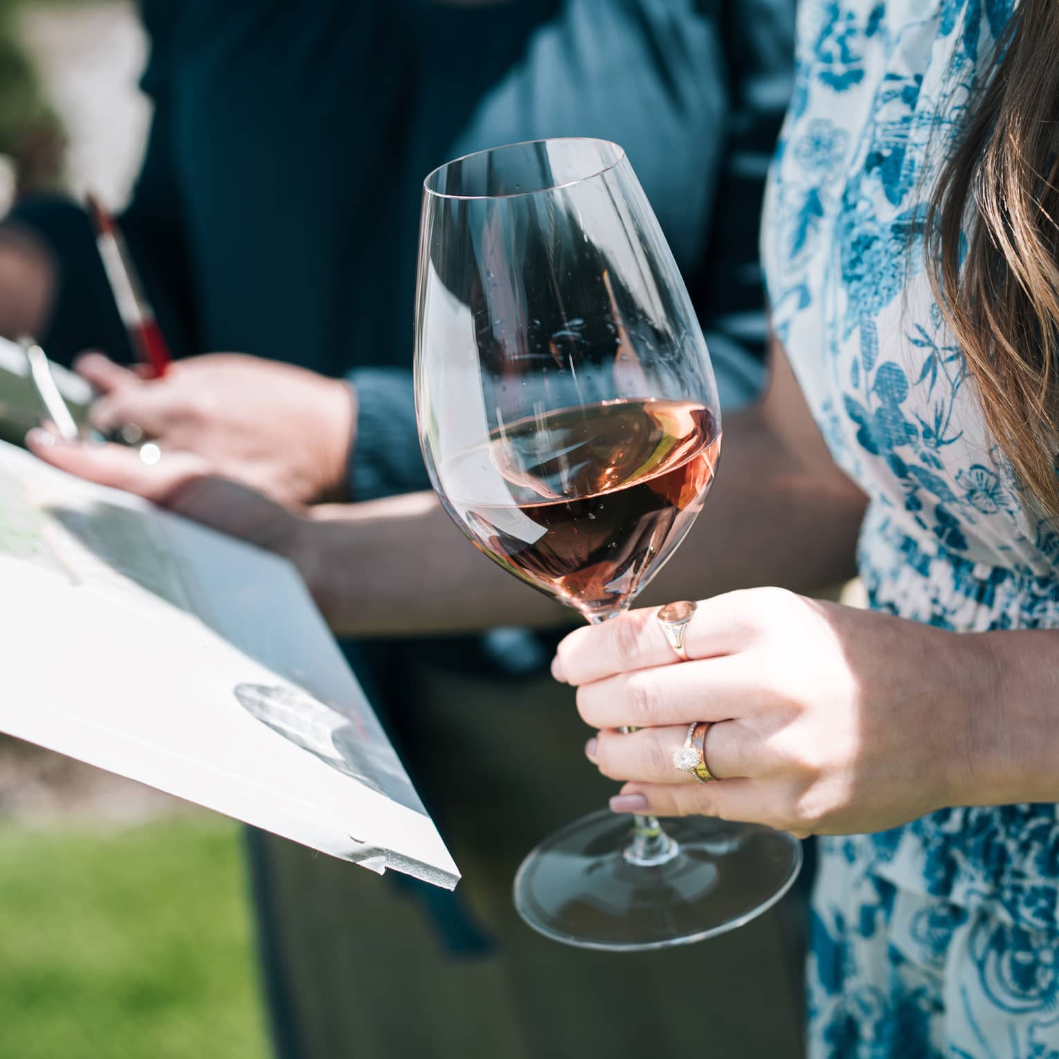 Person holds a glass of wine in one hand while holding a painting in the other