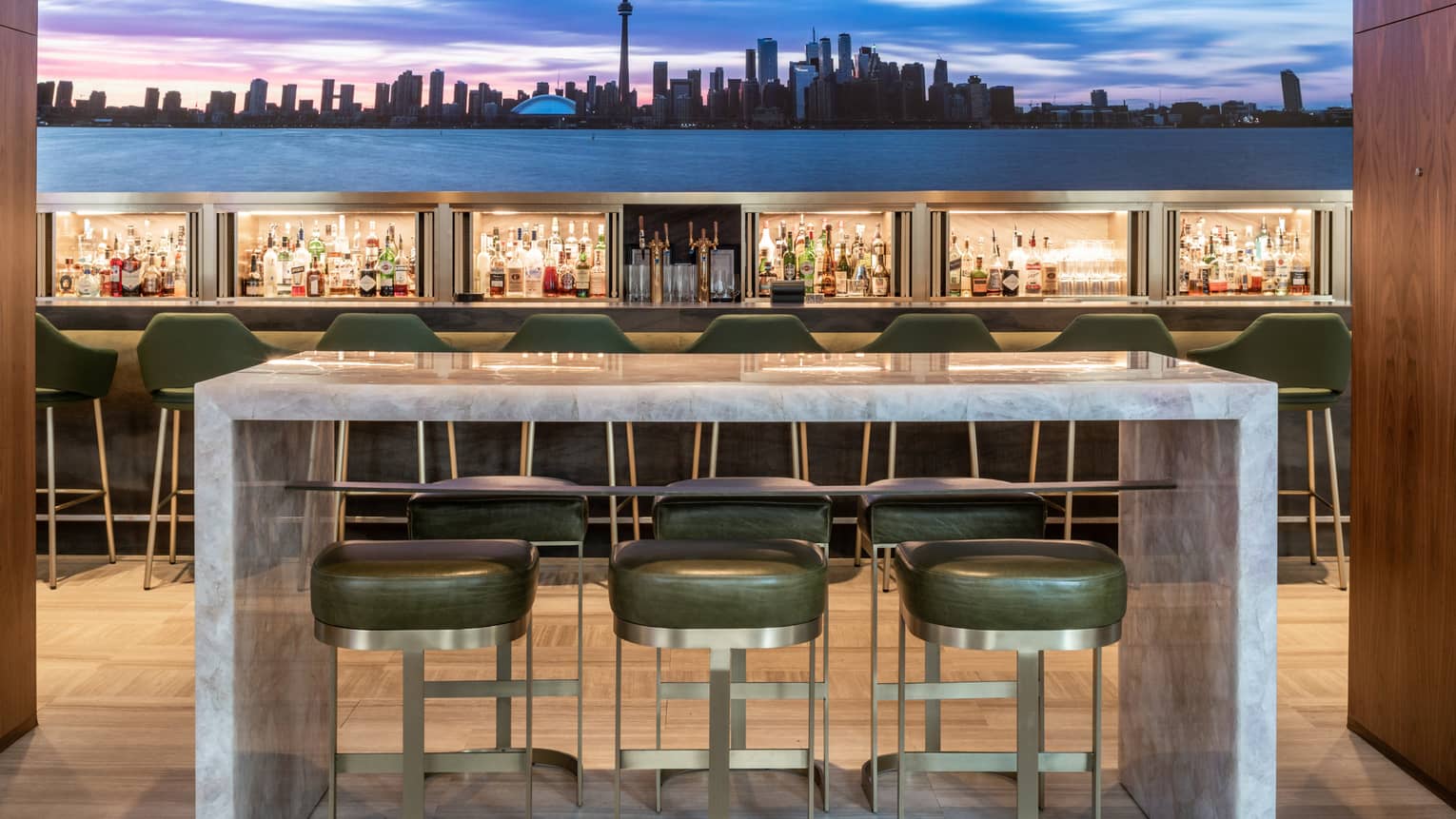 Upholstered high chairs at a marble table near the bar with an image of the skyline behind it