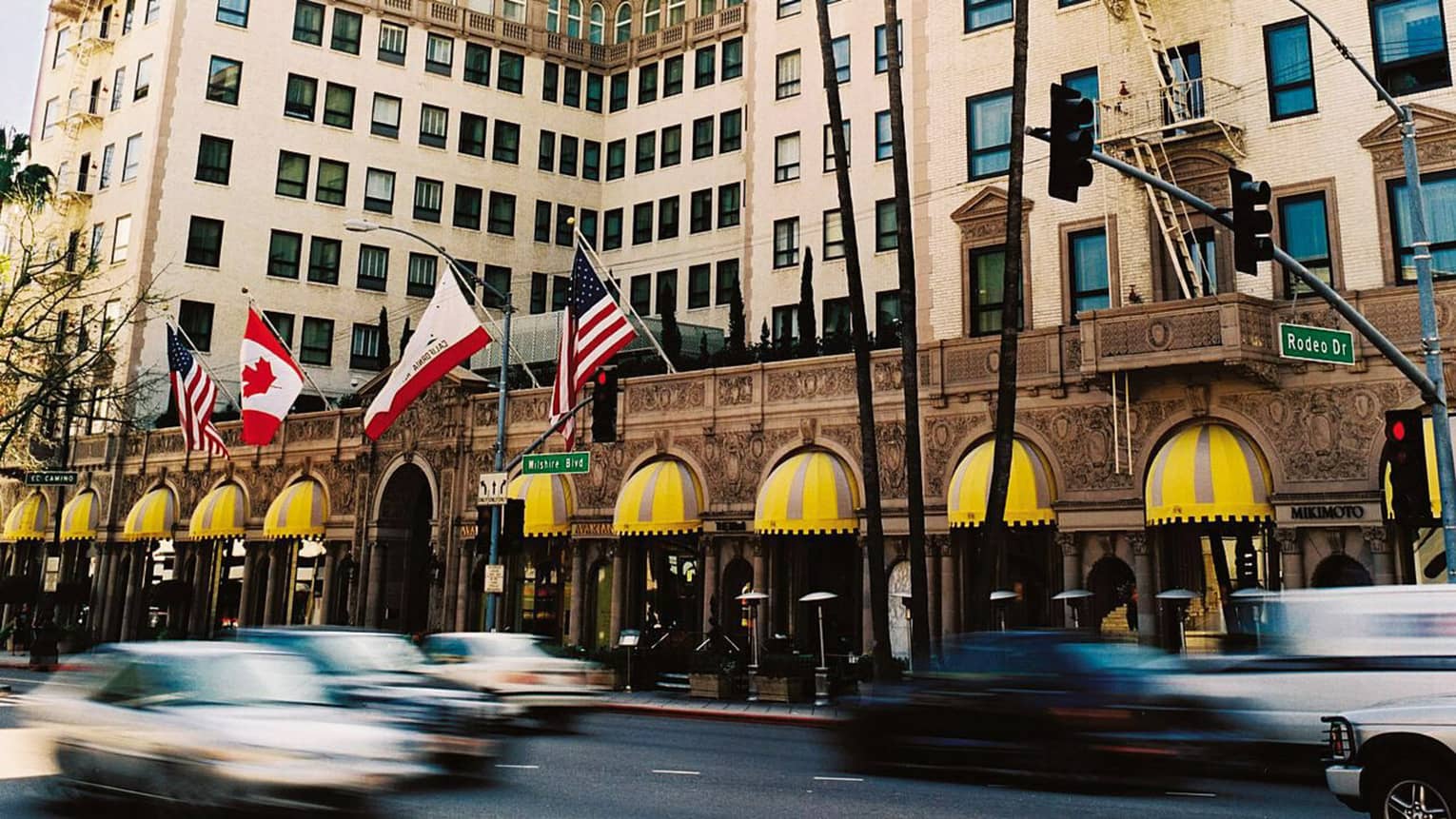 Car drive by the pink four seasons Beverly Wilshire as flags fly in the wind and palm trees sway