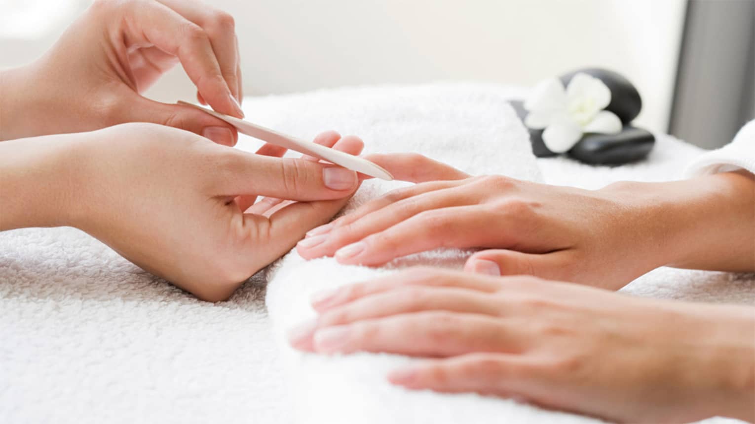 Close-up of spa attendant filing nails of woman's hands as they rest on white towel