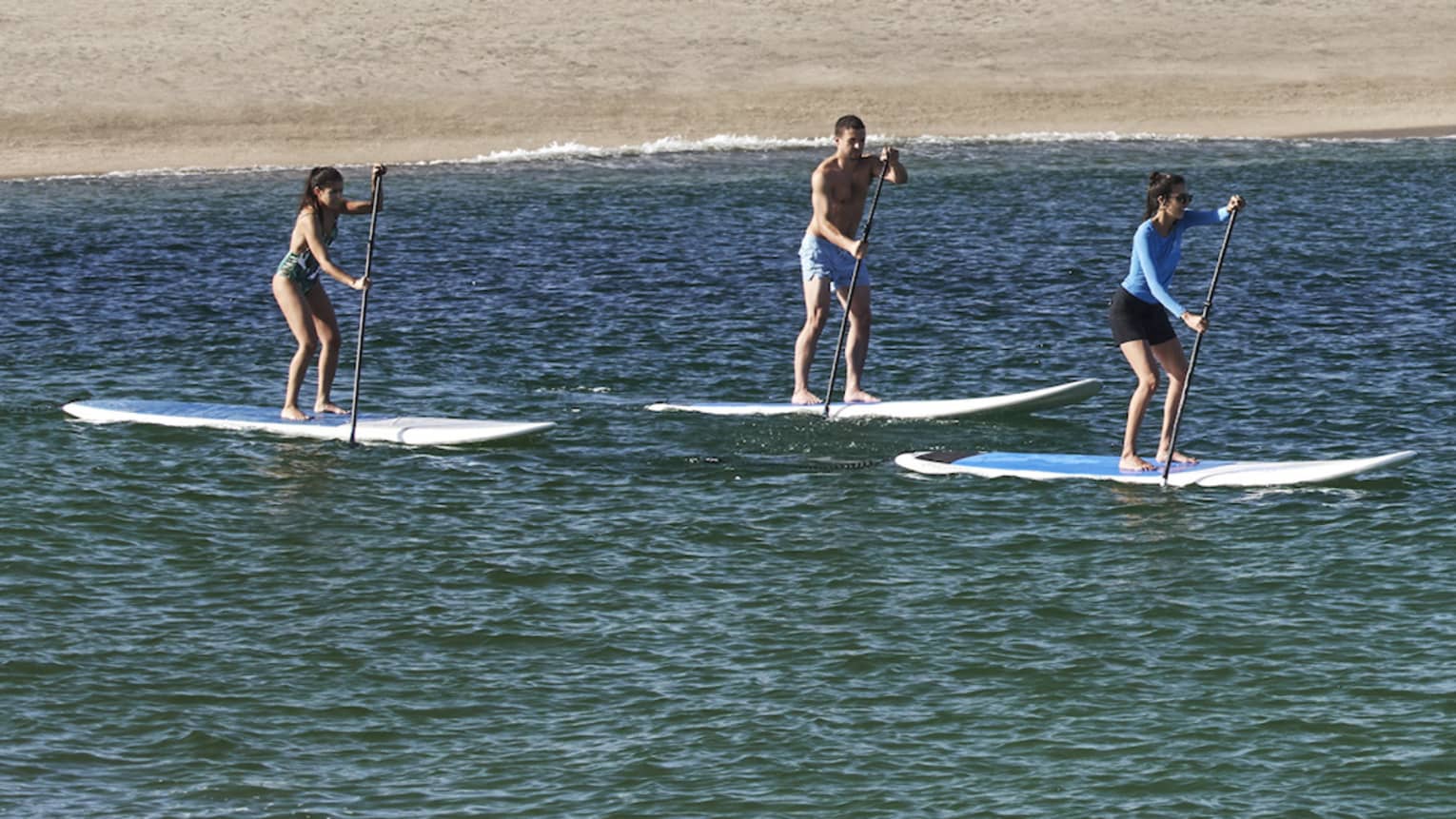 Three people on paddle boards in the water with a hotel behind them.