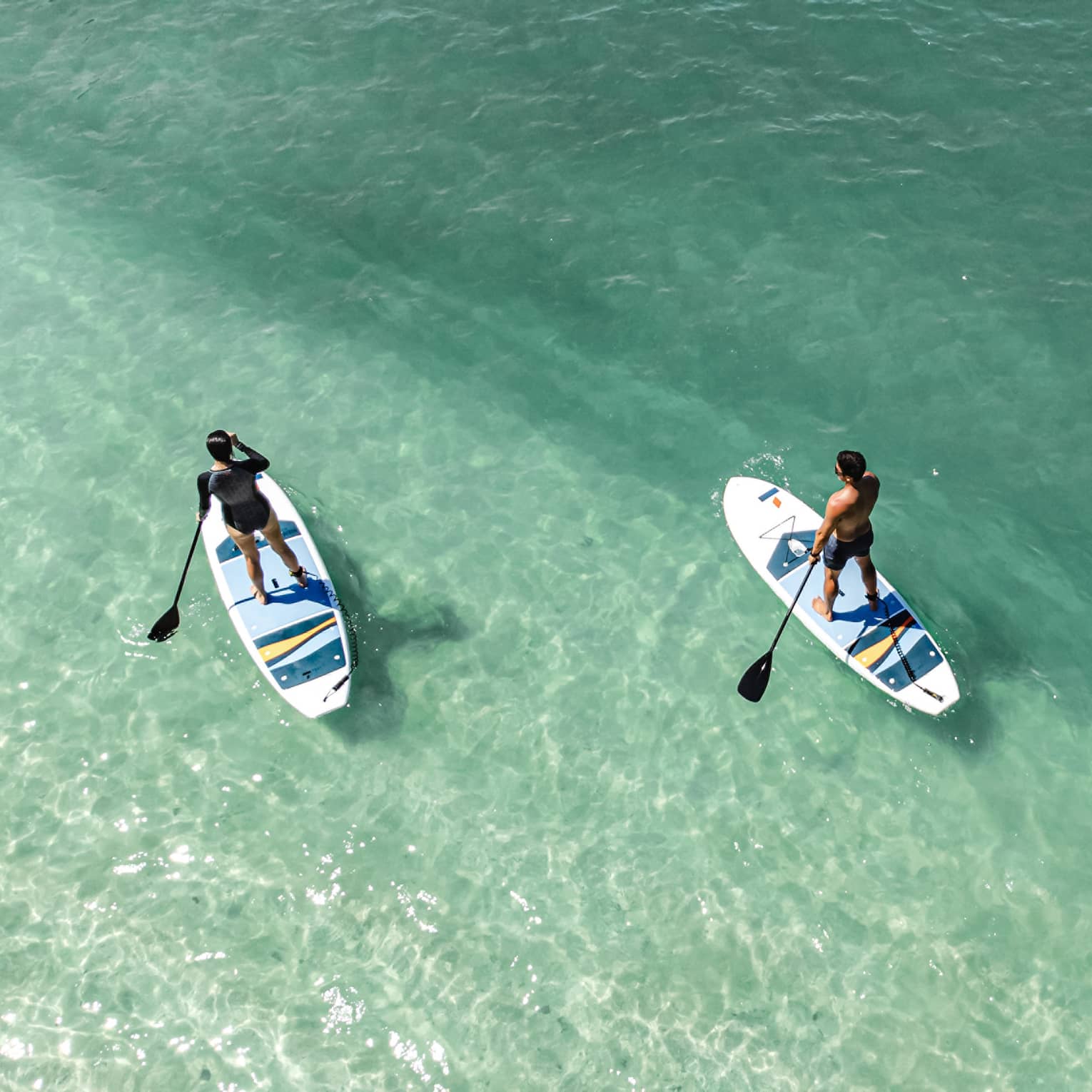 Aerial view of two people paddleboarding in clear green-blue water