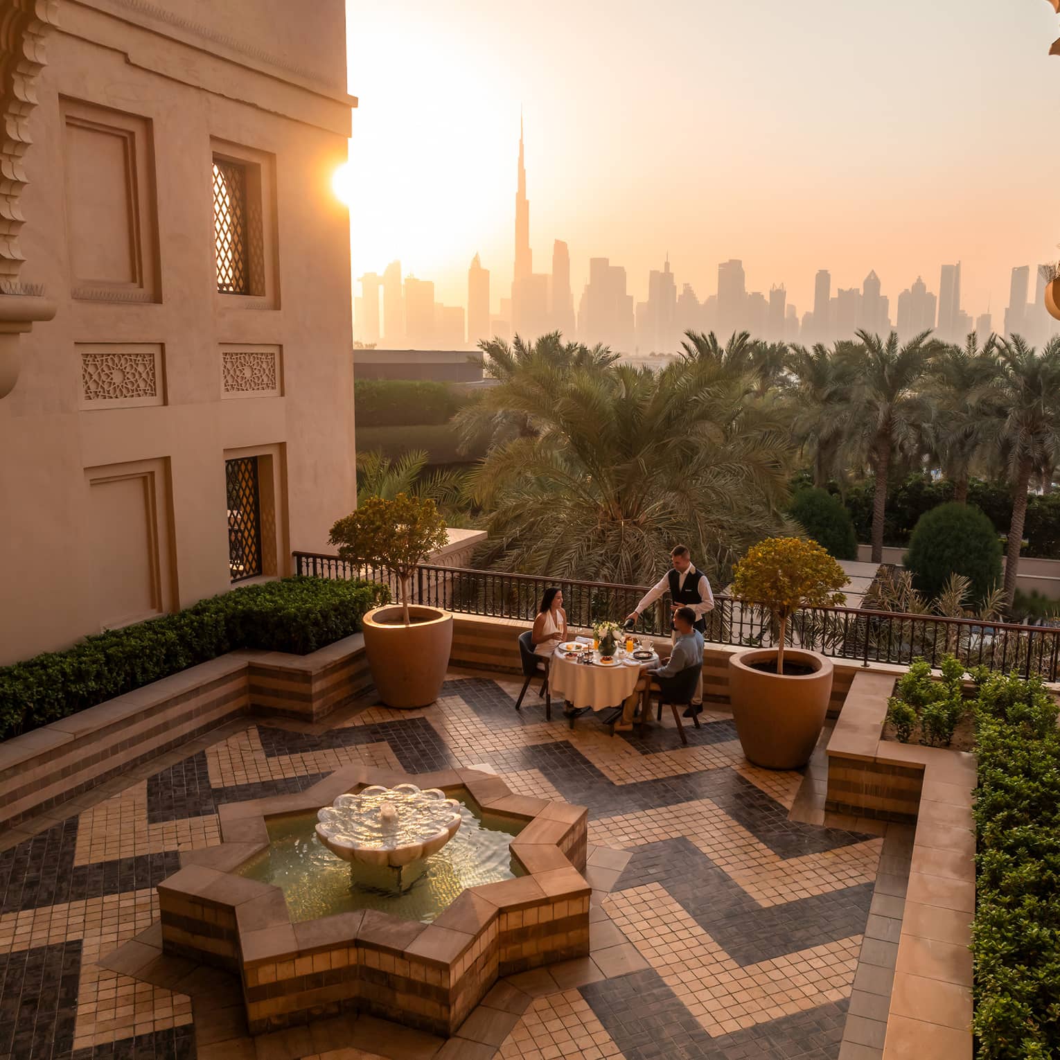 Table set for two on an open-air rooftop terrace with a chevron tiled floor and the sun rising over a city skyline in the near distance
