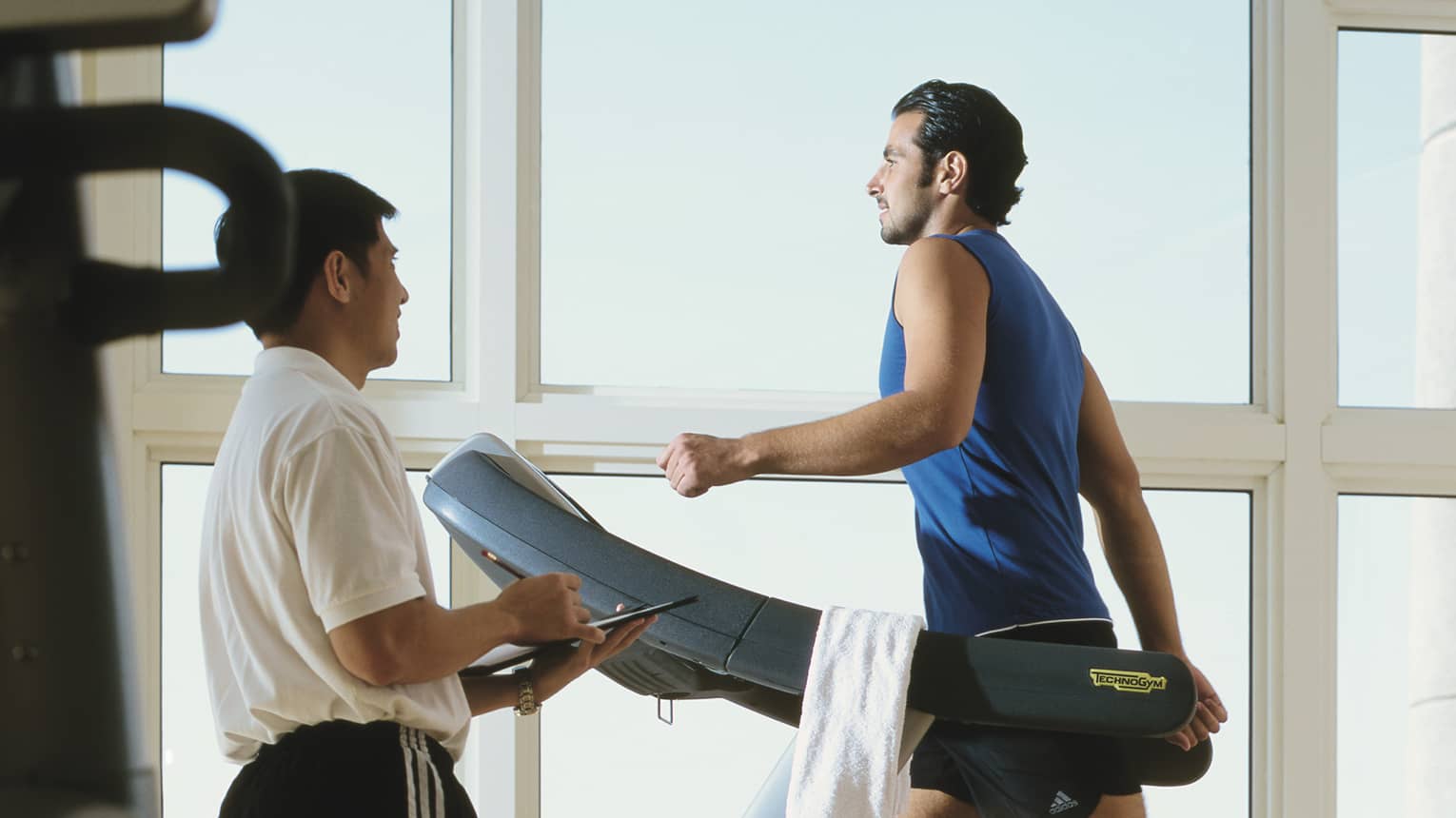 Man in workout gear on treadmill as personal trainer looks on