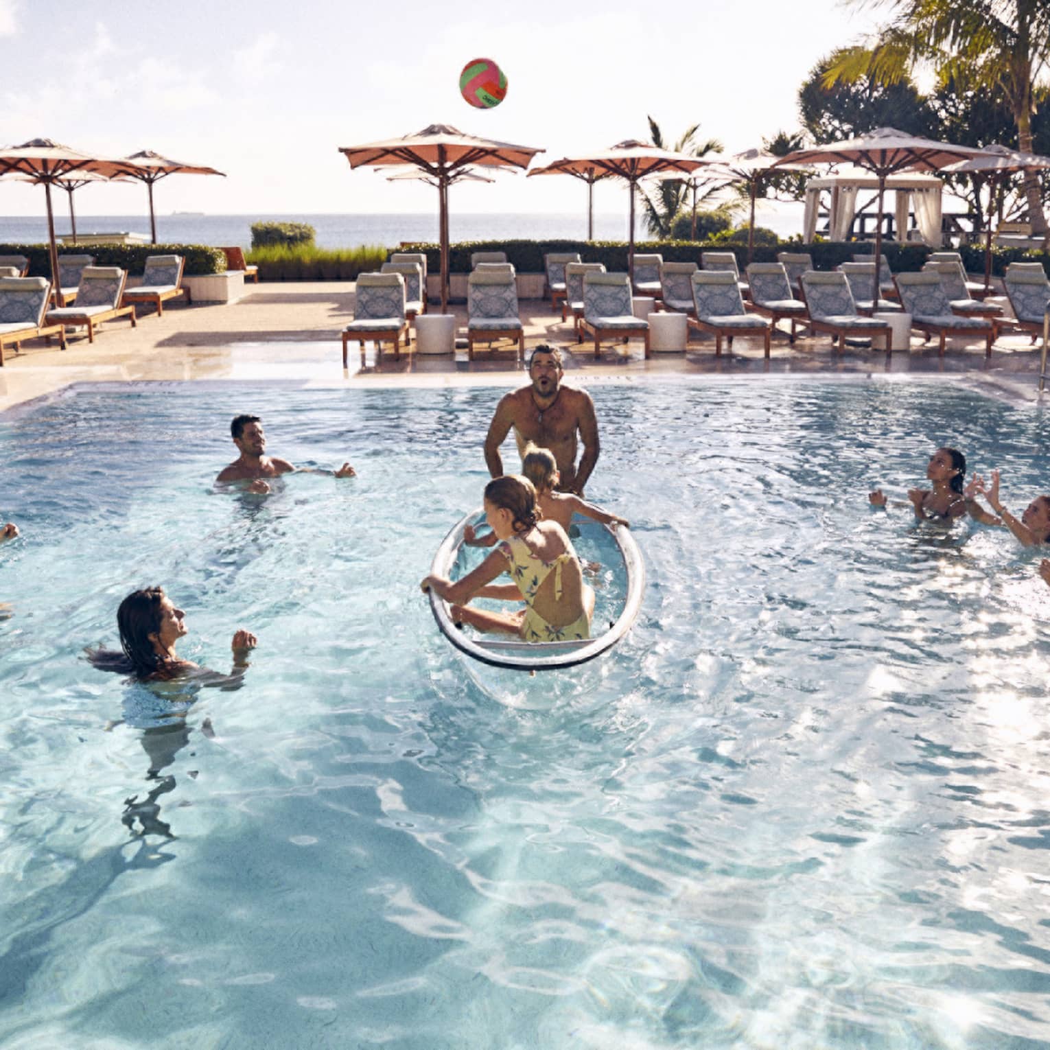 Guests in the pool with palm trees and the ocean in the background.