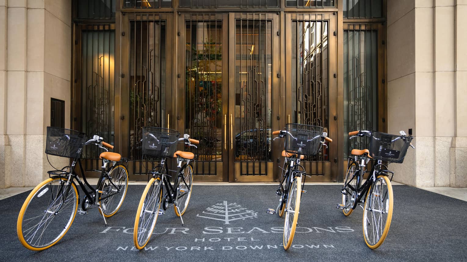 Four identical bicycles sit at the Hotel's exterior, the rug underneath displaying the Four Seasons logo