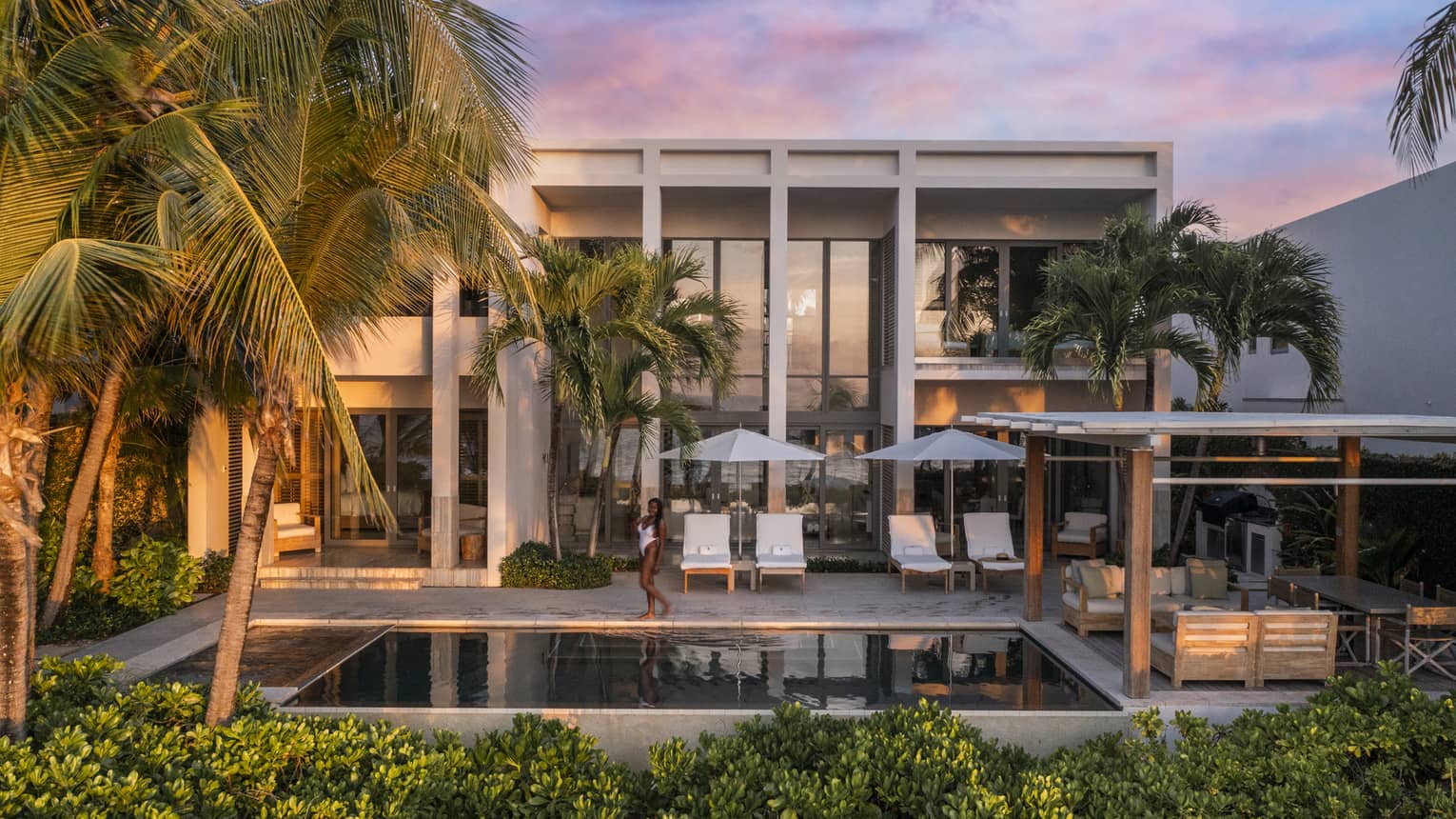 Beachfront villa at sunset, featuring a private pool, lounge chairs and tropical greenery, with a guest enjoying the serene surroundings at a luxury resort