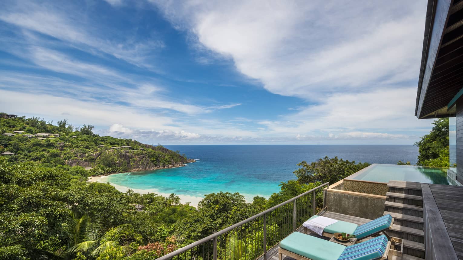 Blue lounge chairs on balcony overlooking lush mountain, beach, ocean, blue sky