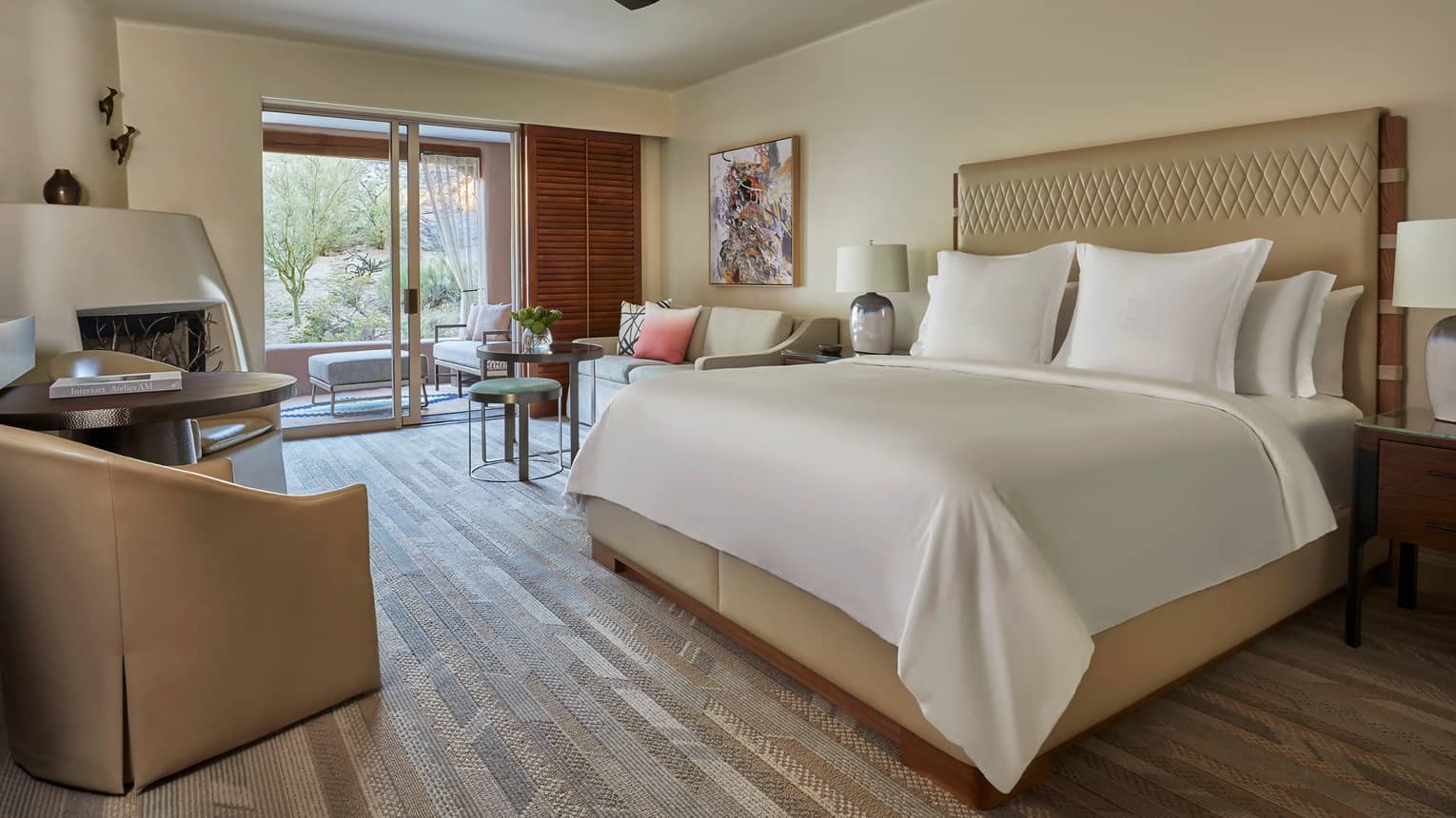 King-bedded room with wooden floors, arm chair, ceiling fan and walk-out patio