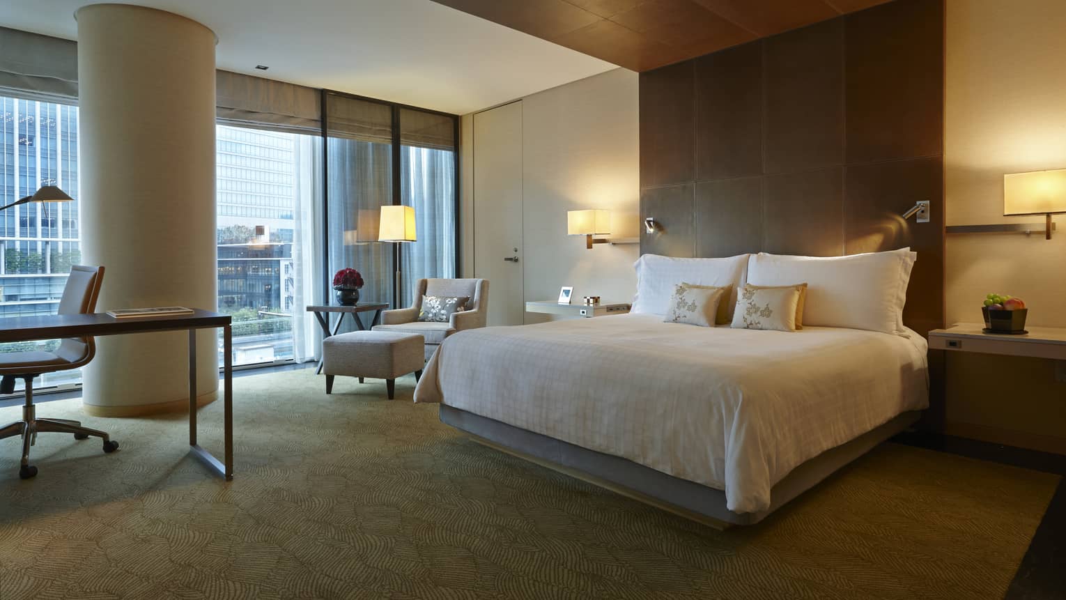 Deluxe King Room bed by modern wood panel wall, desk, chair by white pillar, window