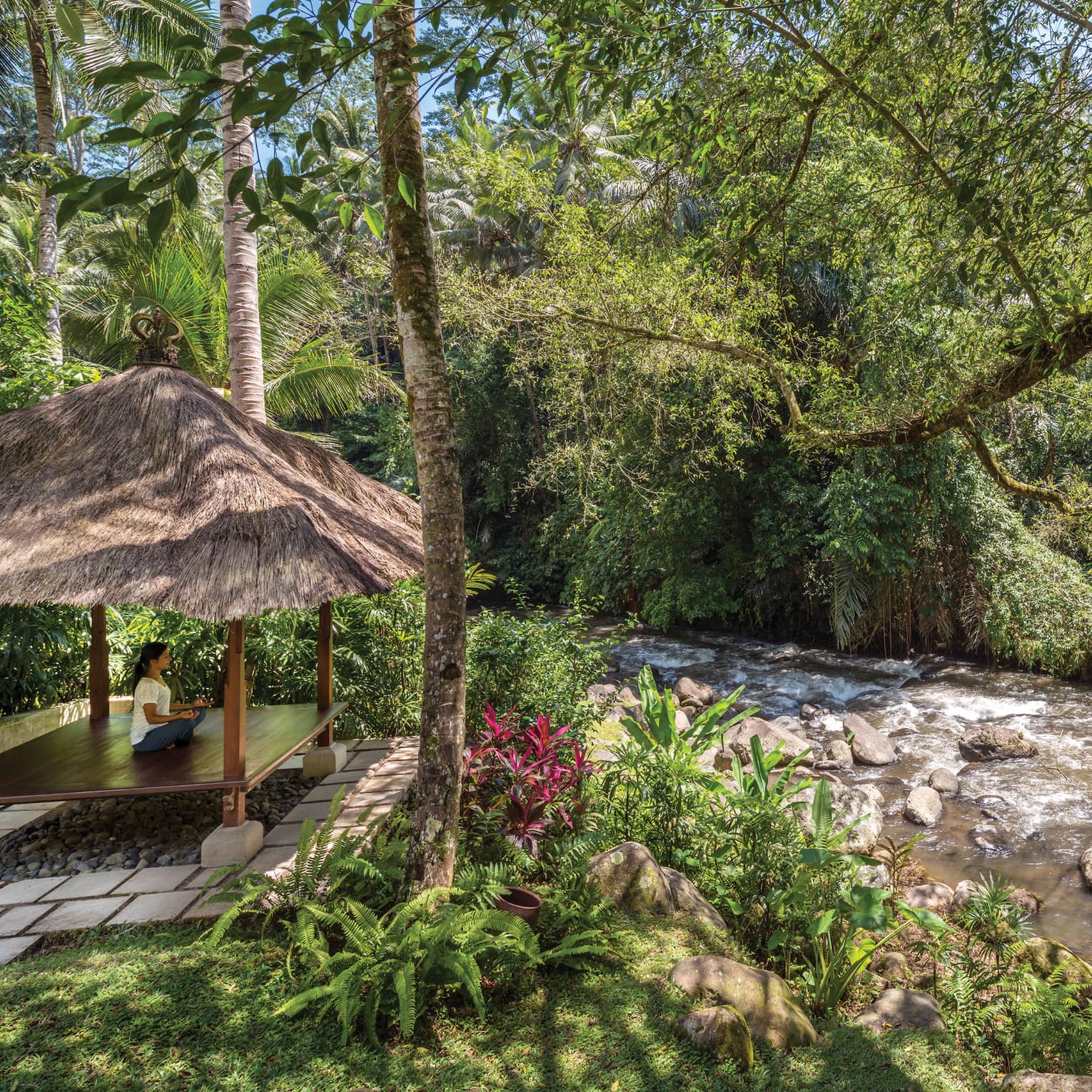 A guest meditating in a pavilion next to a flowing river in Bali