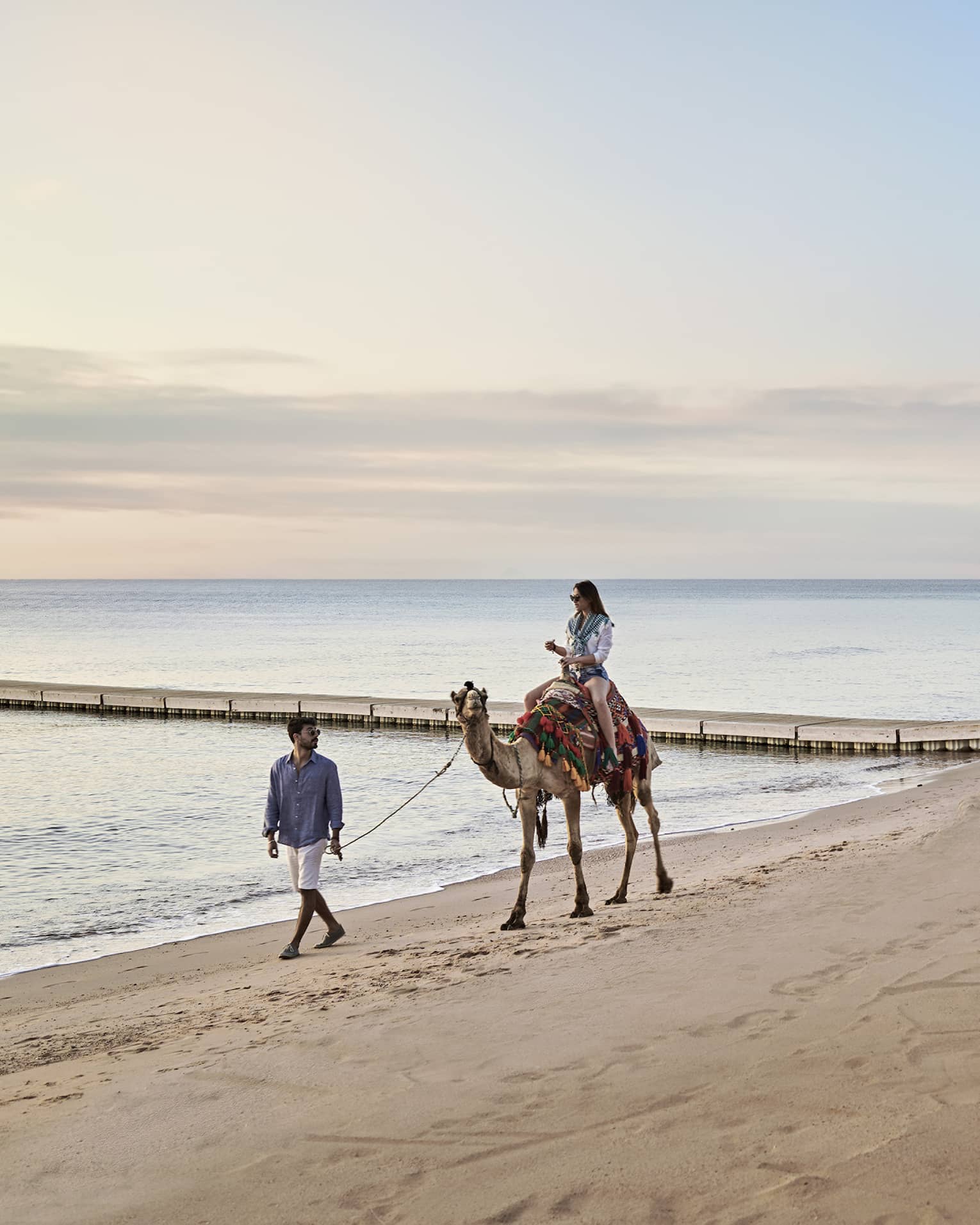 A woman rides a camel, led by a man, along the beach at Four Seasons Sharm El Sheikh