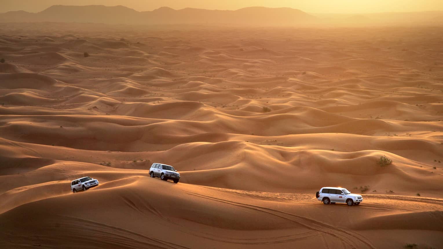 Aerial view of three Sundowner Desert Safari utility vehicles driving over sand dunes
