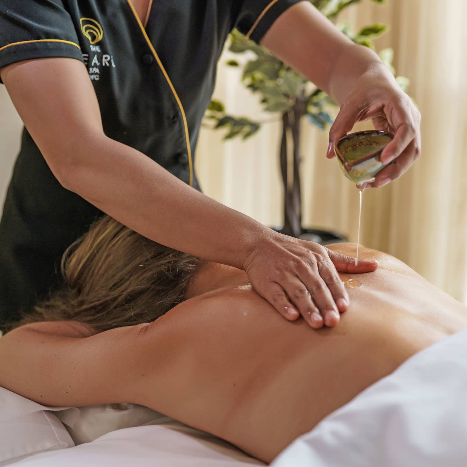 Guest lies face down an a massage table covered in a white cloth as a masseuse spreads oil on the guest's back