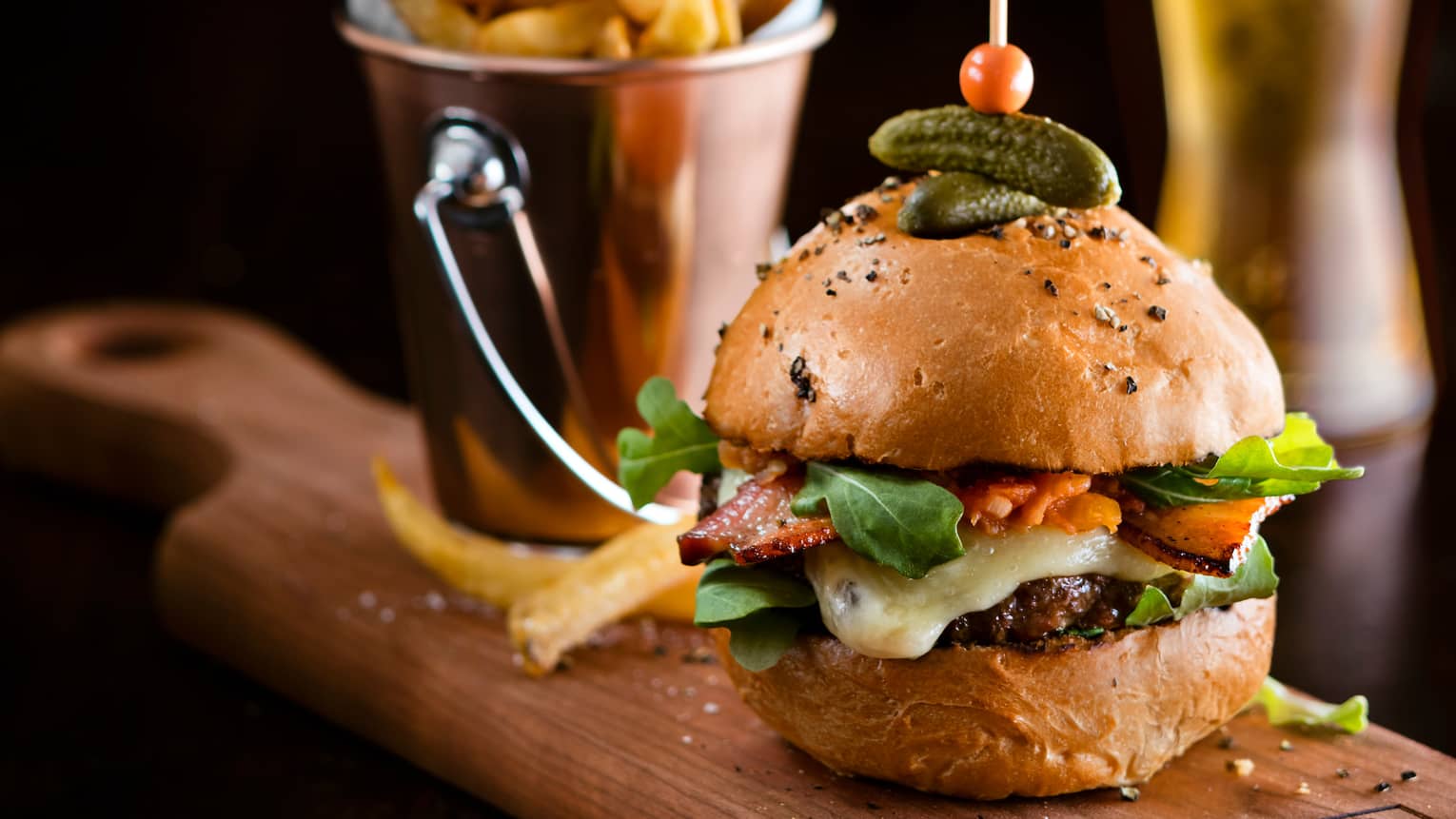 Burger with melted cheese, lettuce and tomato on rustic bun with dill pickle spear, bucket of French fries