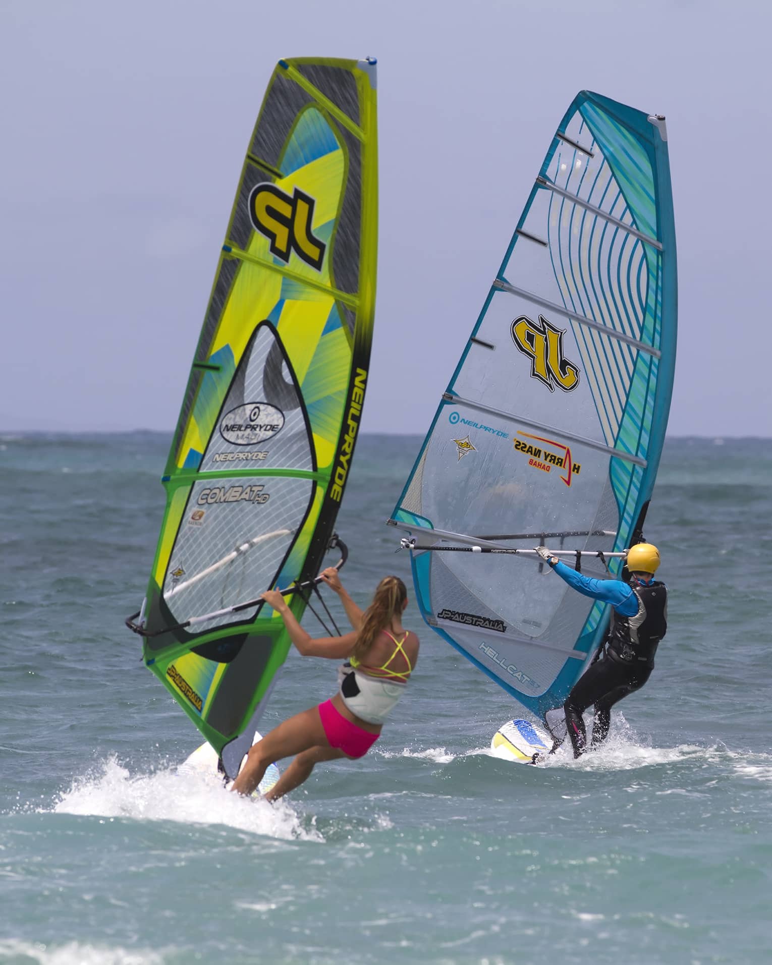 Two windsurfers leaning into the open sea under an azure blue sky, each creating a small wake.