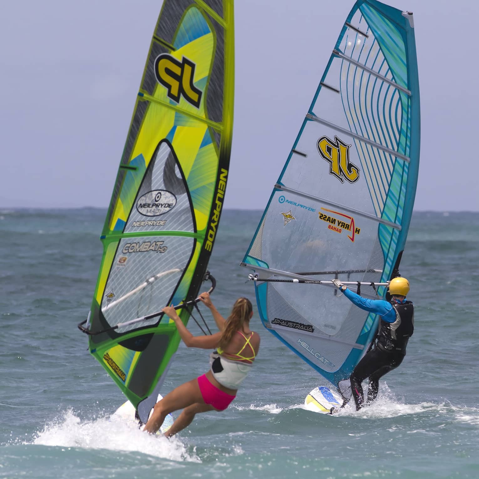 Two windsurfers leaning into the open sea under an azure blue sky, each creating a small wake.