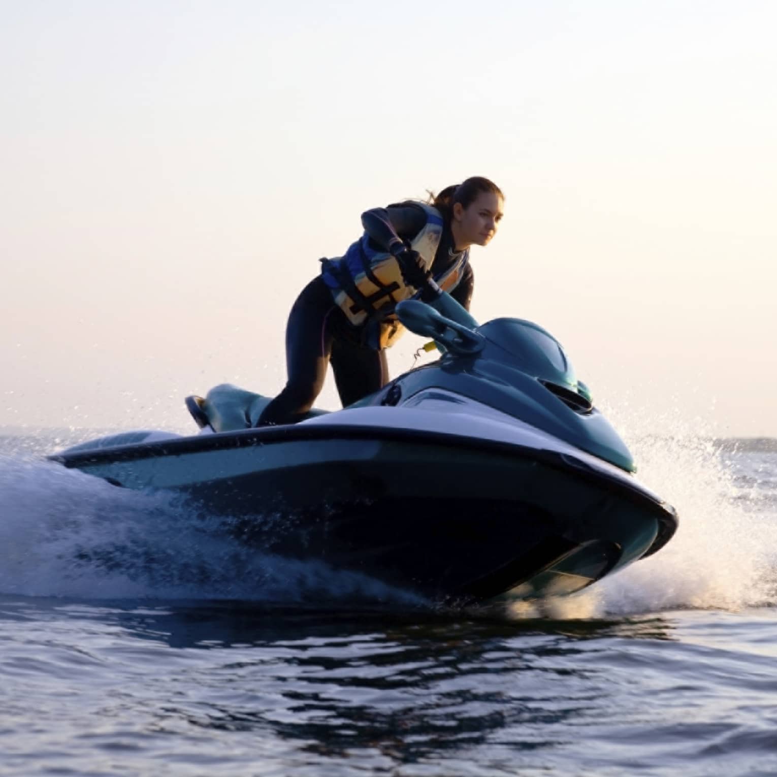 Woman wearing life jacket stands, steers jet ski on ocean at sunset