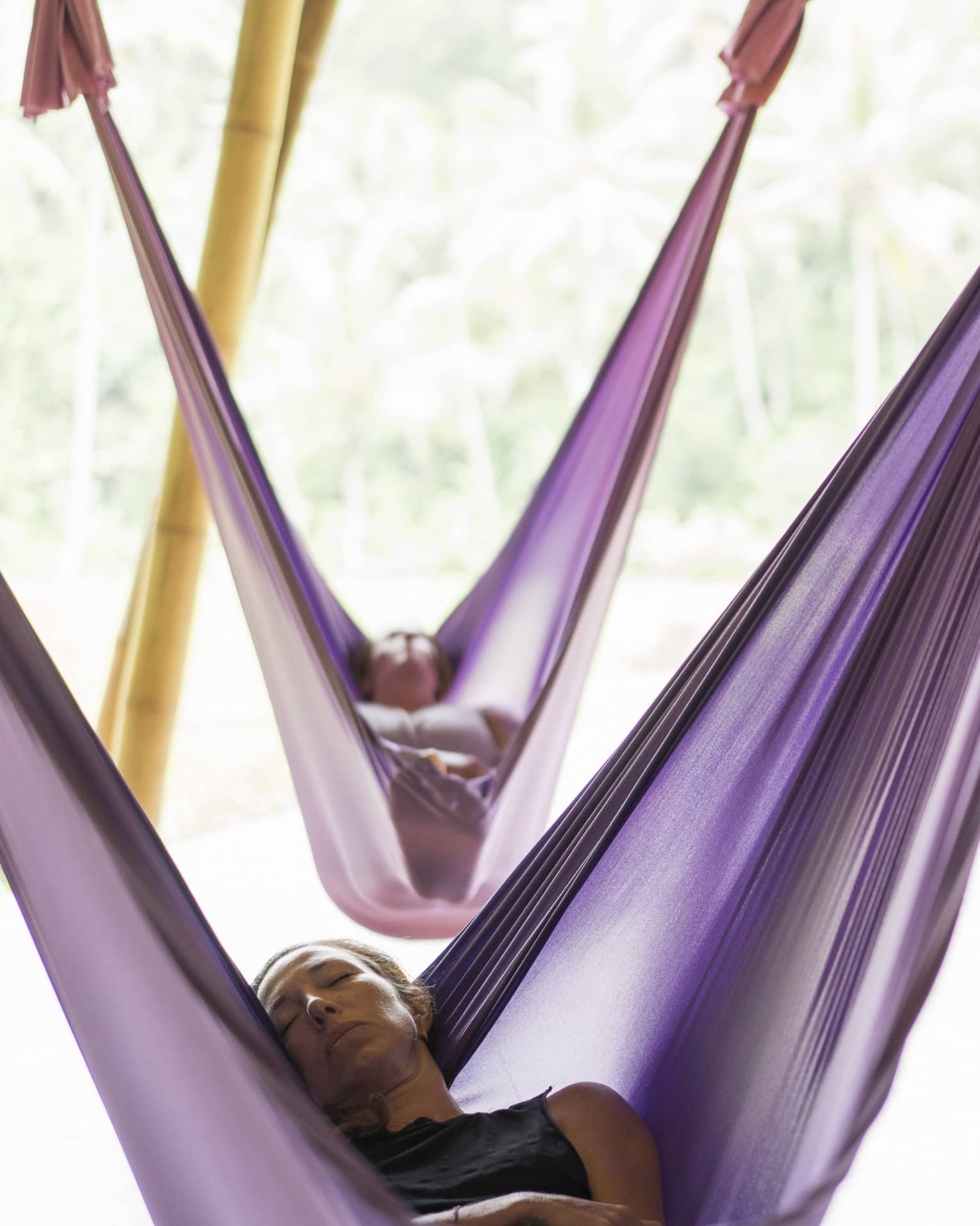 Guests nap in hanging silk hammocks while an instructor plays a sound bowl.
