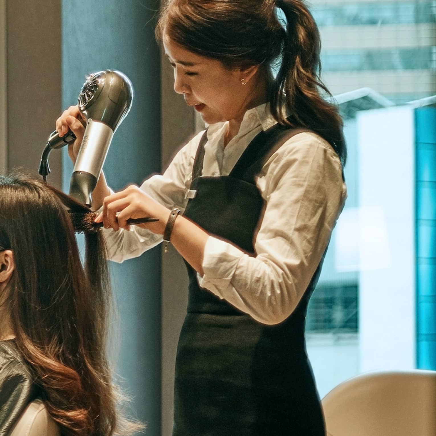 Hair stylist blow dries woman's hair in hotel salon