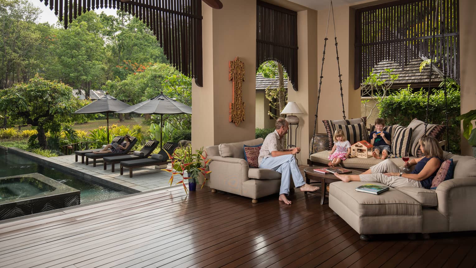 A family sits on an L-shaped couch overlooking a private pool and cabana.