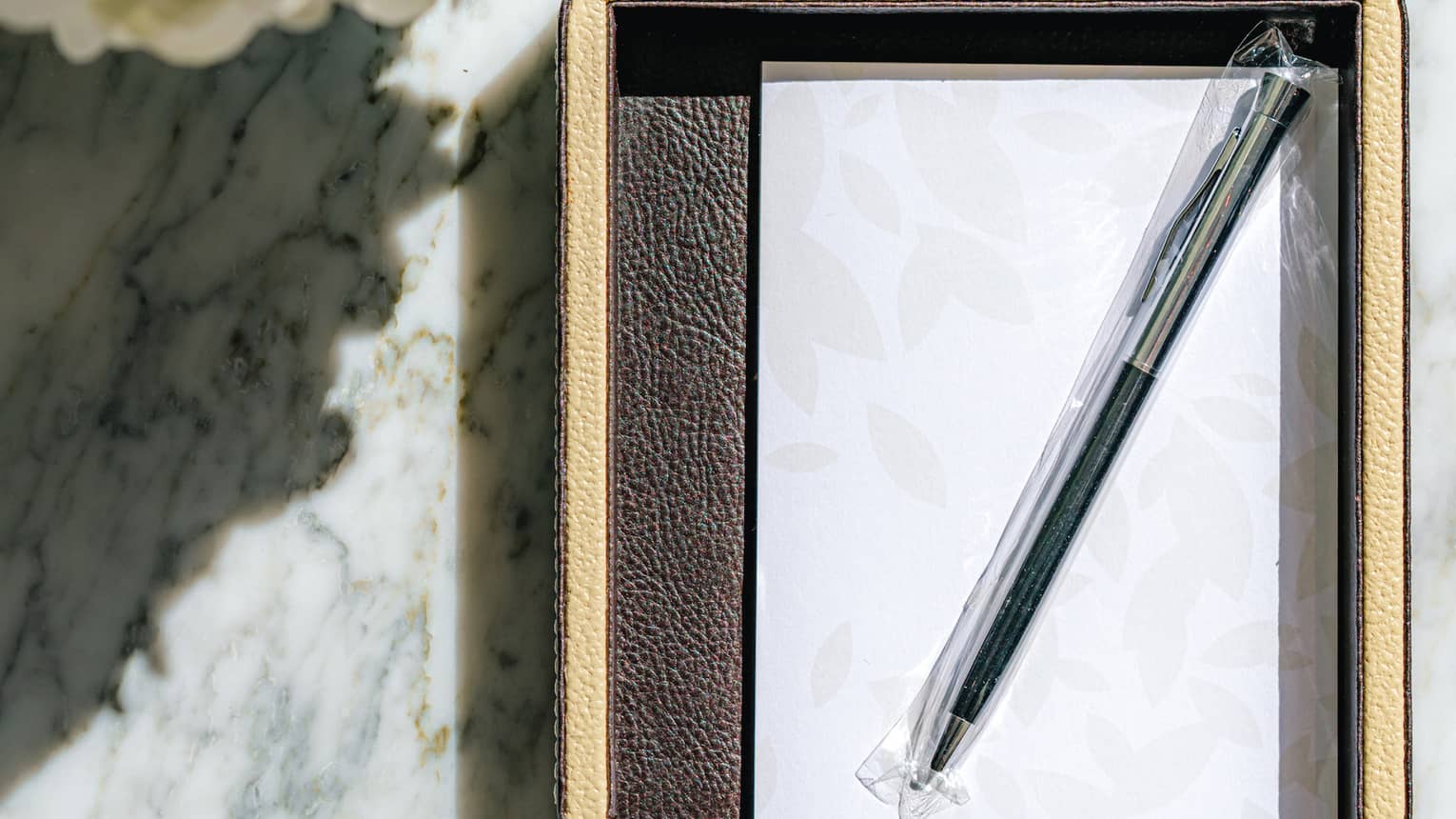 A notepad and pen sit on marble table next to bouquet of flowers
