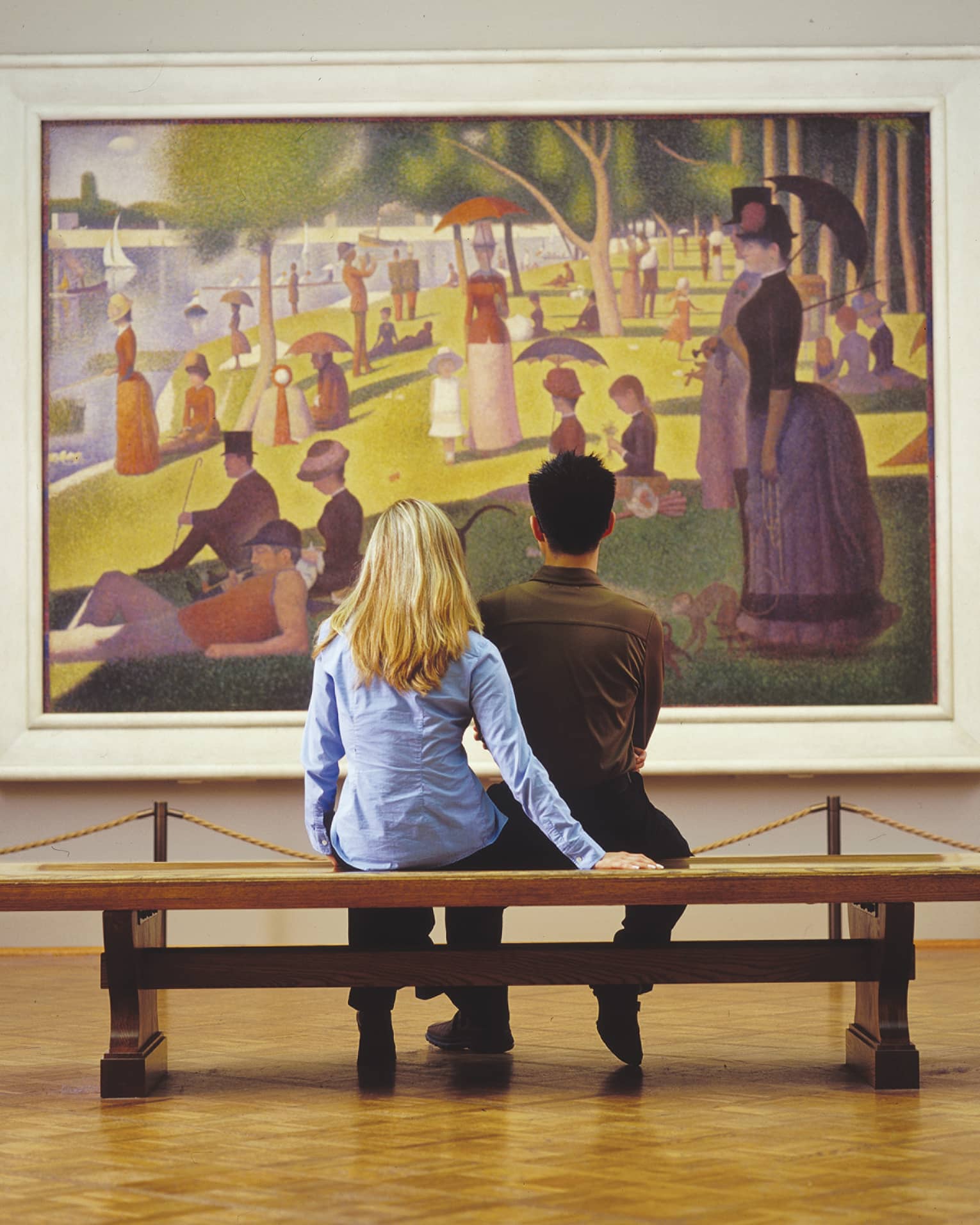 A couple admiring Seurat's iconic Pointillist painting, A Sunday on La Grande Jatte, depicting people strolling in a park.