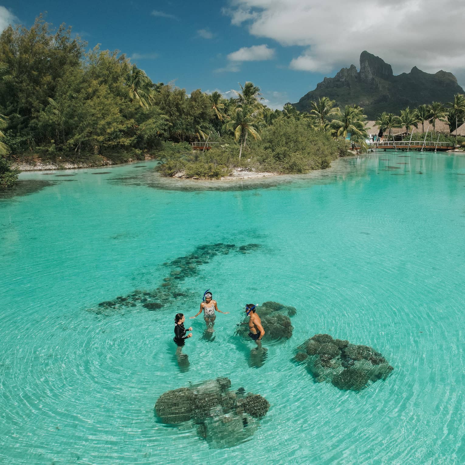 Aerial view of three guests standing in the clear turquoise water of the lagoon at the Dive Centre