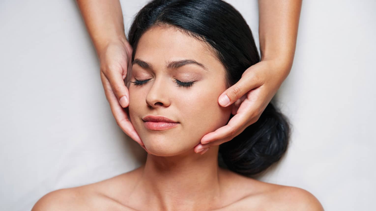 Woman with eyes closed as hands massage her face