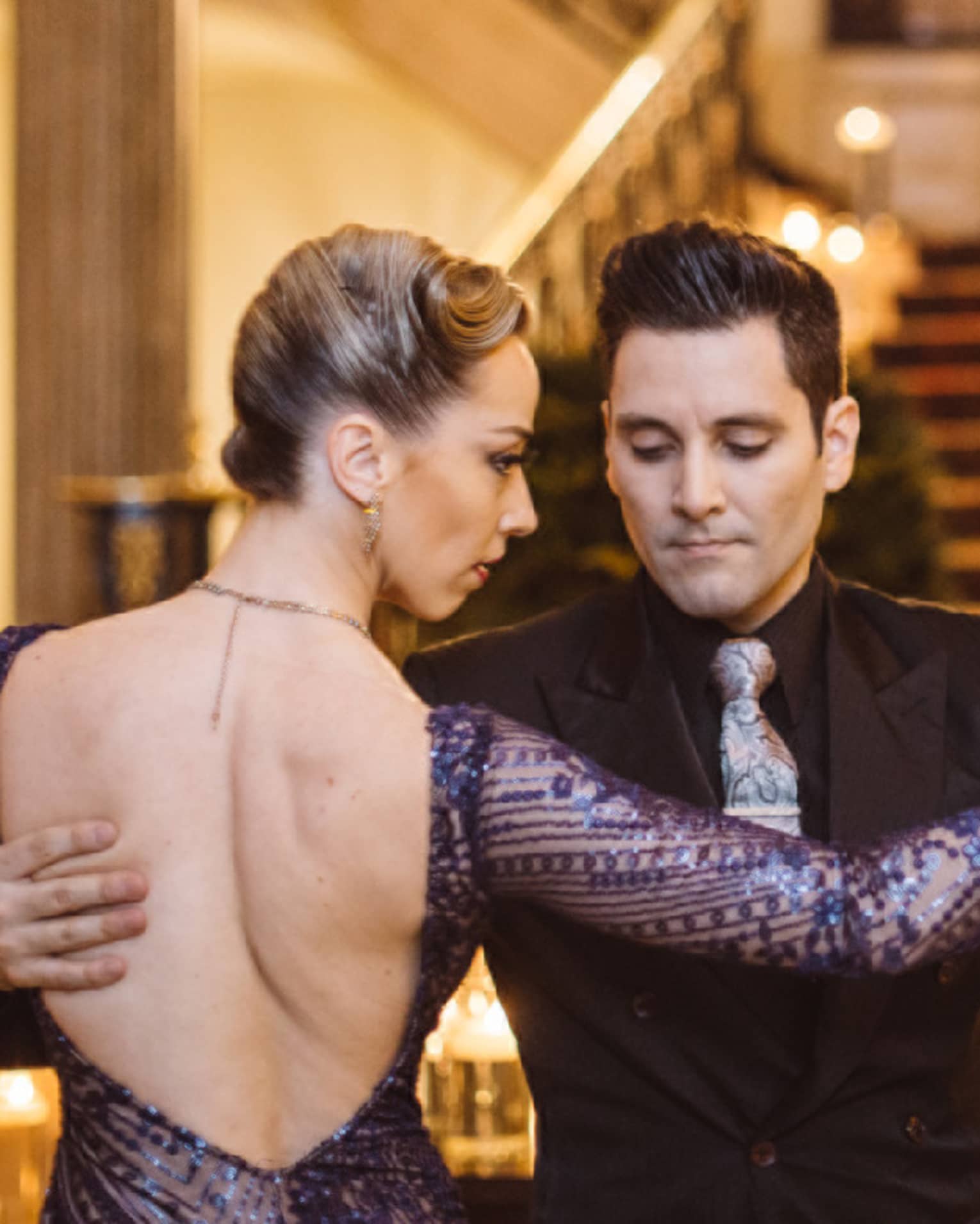 A man and woman tango dancing at the bottom of a wide red carpeting stairway