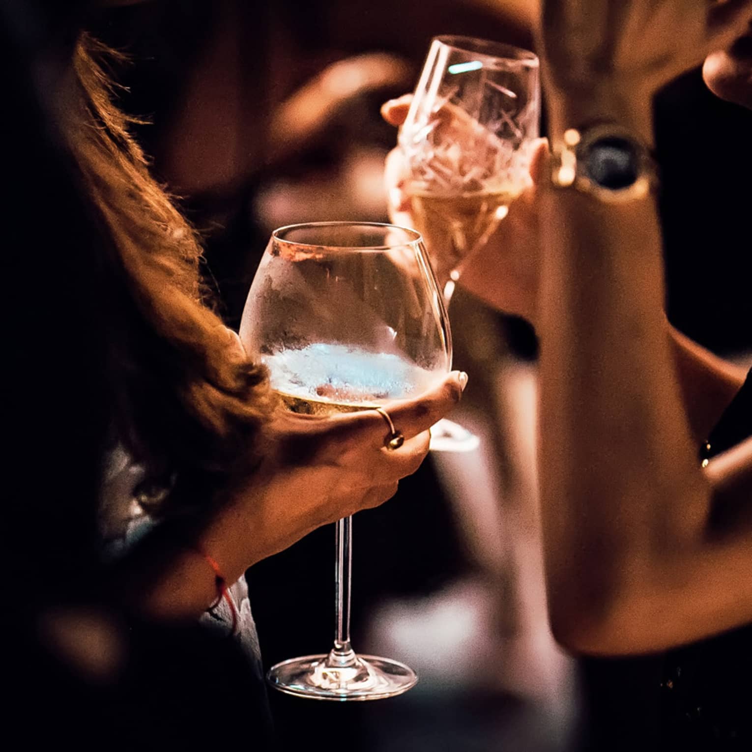 Close-up of women's hands holding wine, cocktail glasses in dark lounge