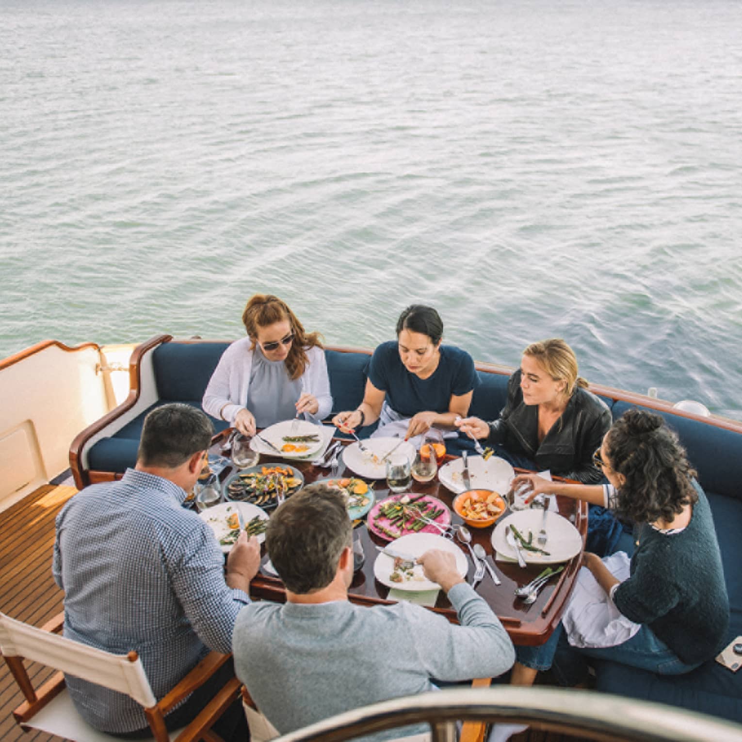 Group of friends dine at table at end of boat on water 