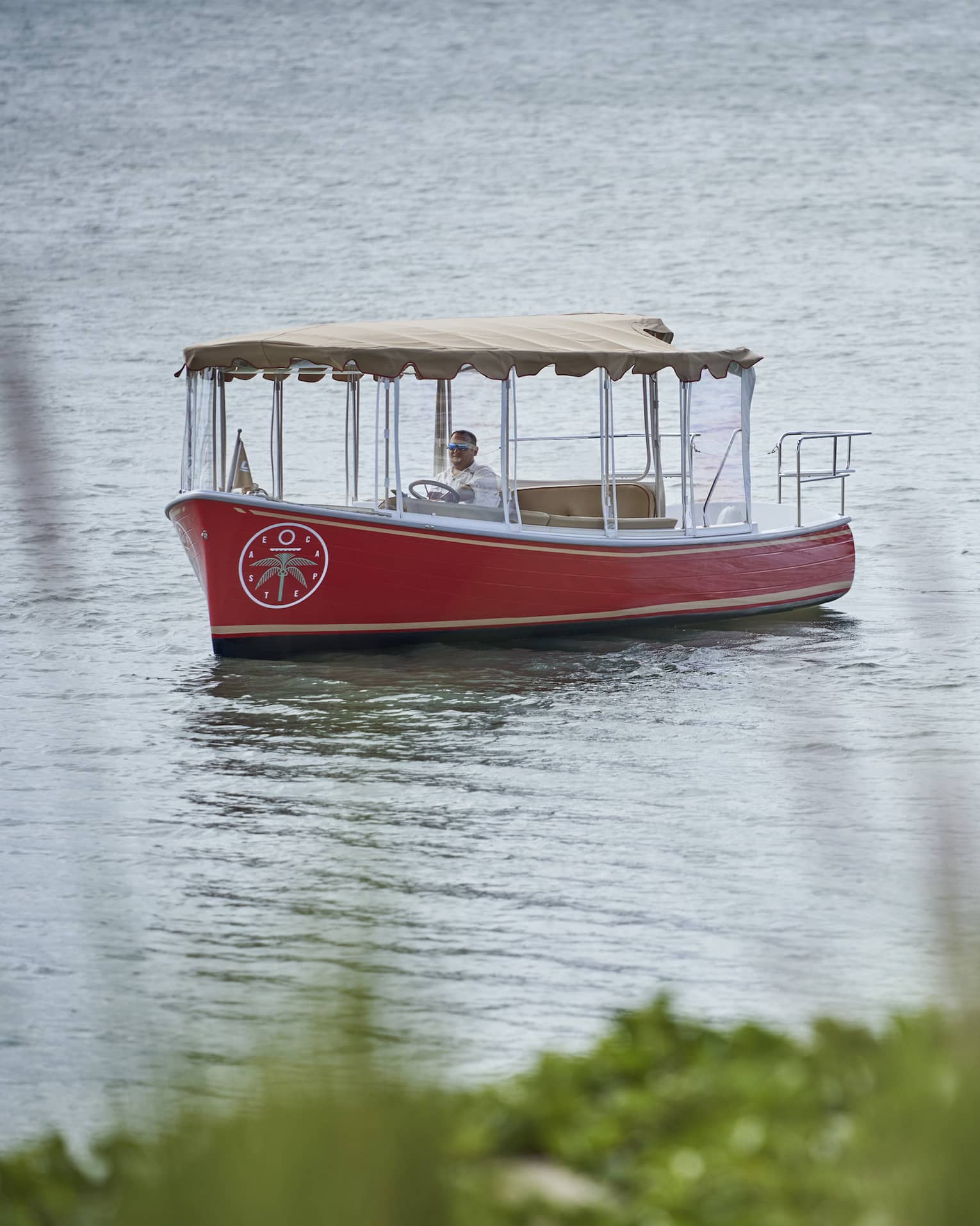 Small red boat with a tan awning floats down a river