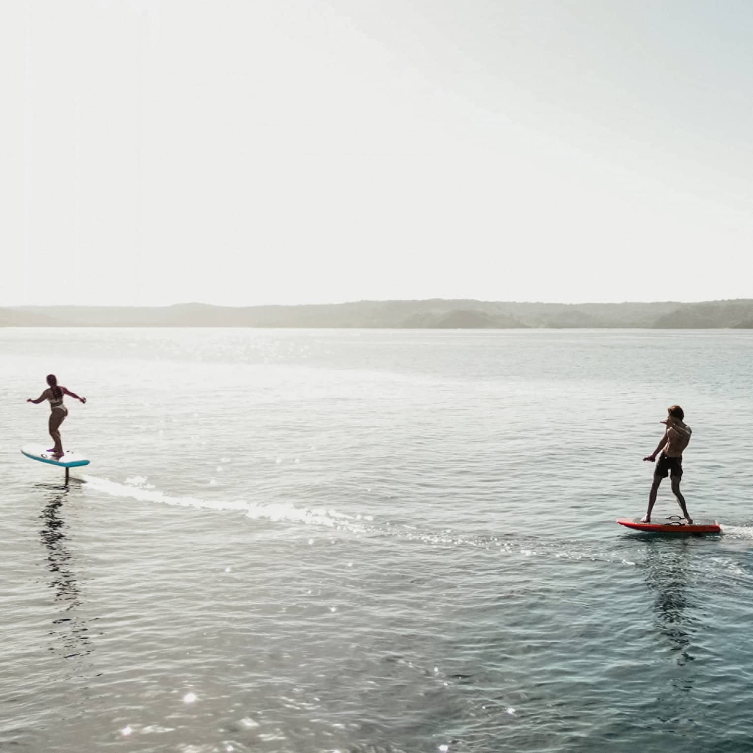 Two silhouetted figues riding e-foil surfboards in the water
