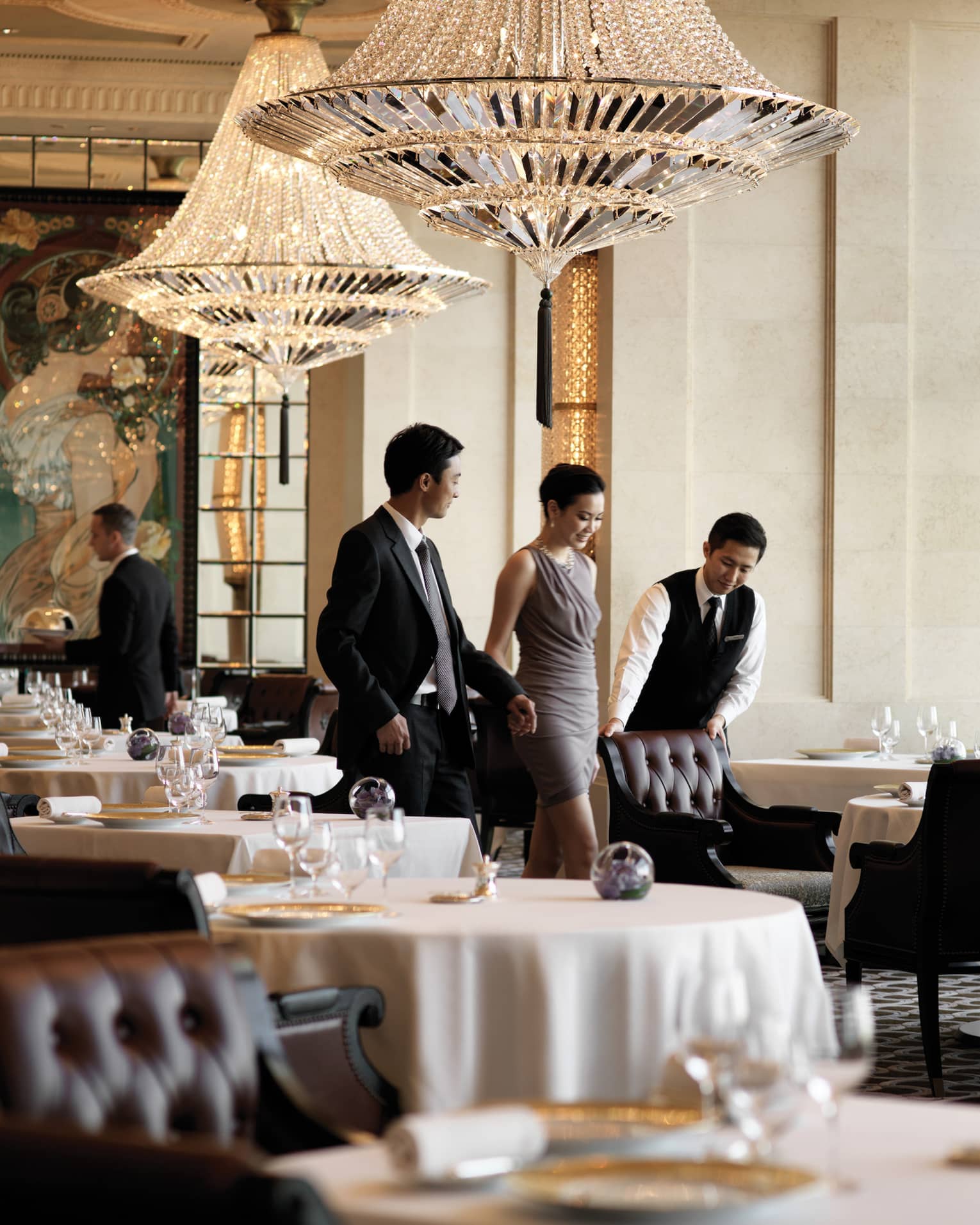 A male waiter pulls a leather seat out at a dining table for a woman