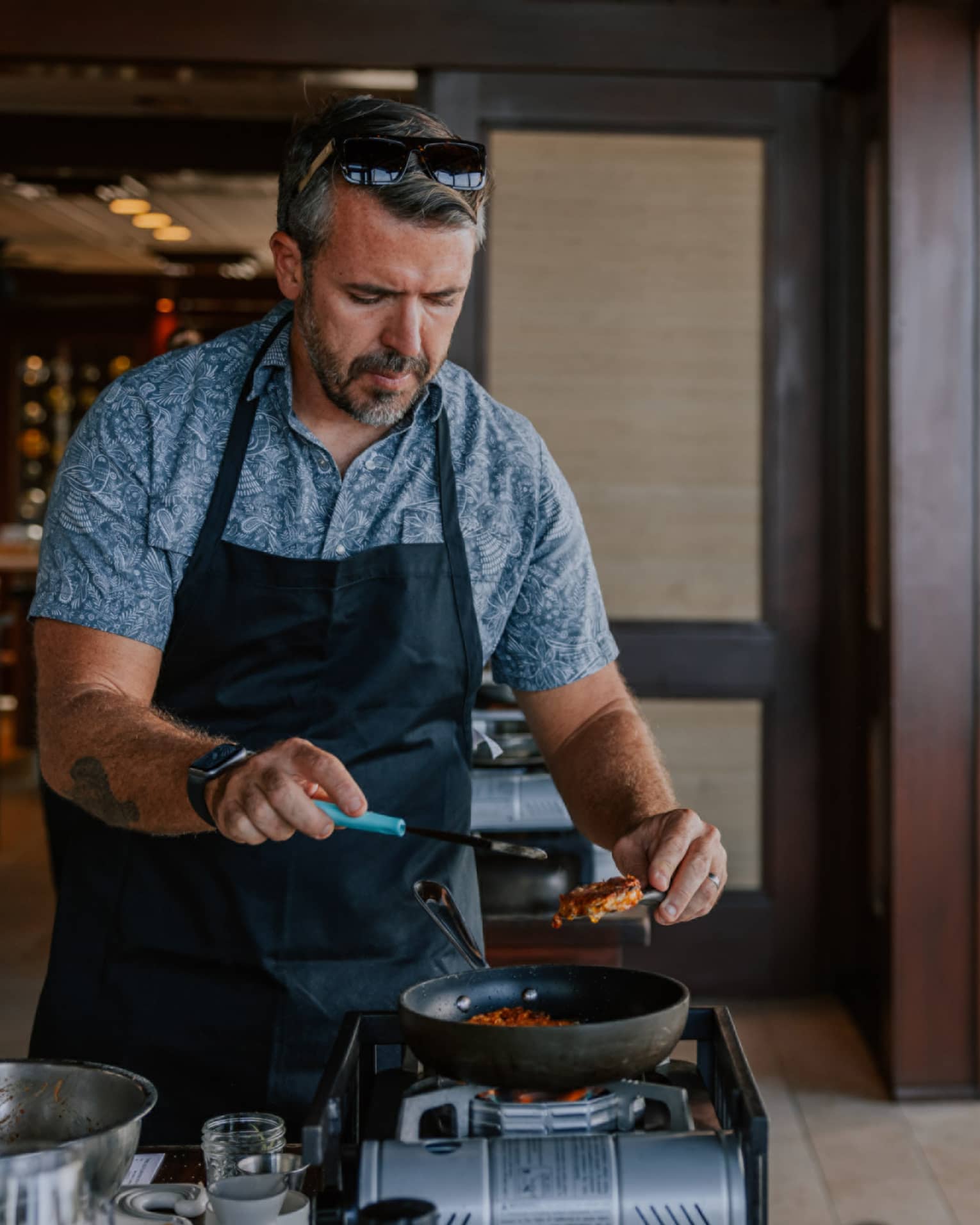 Man wear black apron cooks over a burner