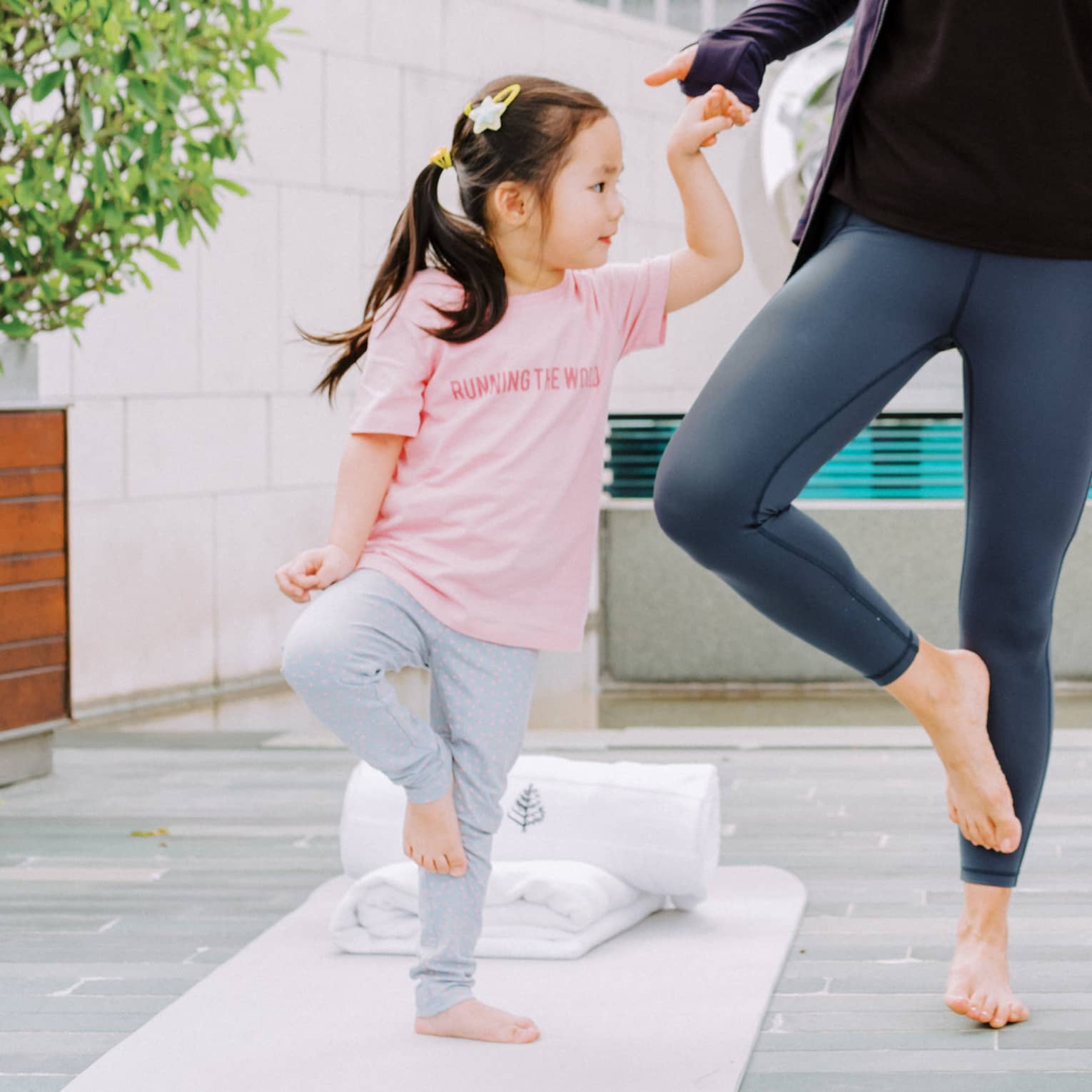 A mother and two young daughters laughing while doing yoga together.